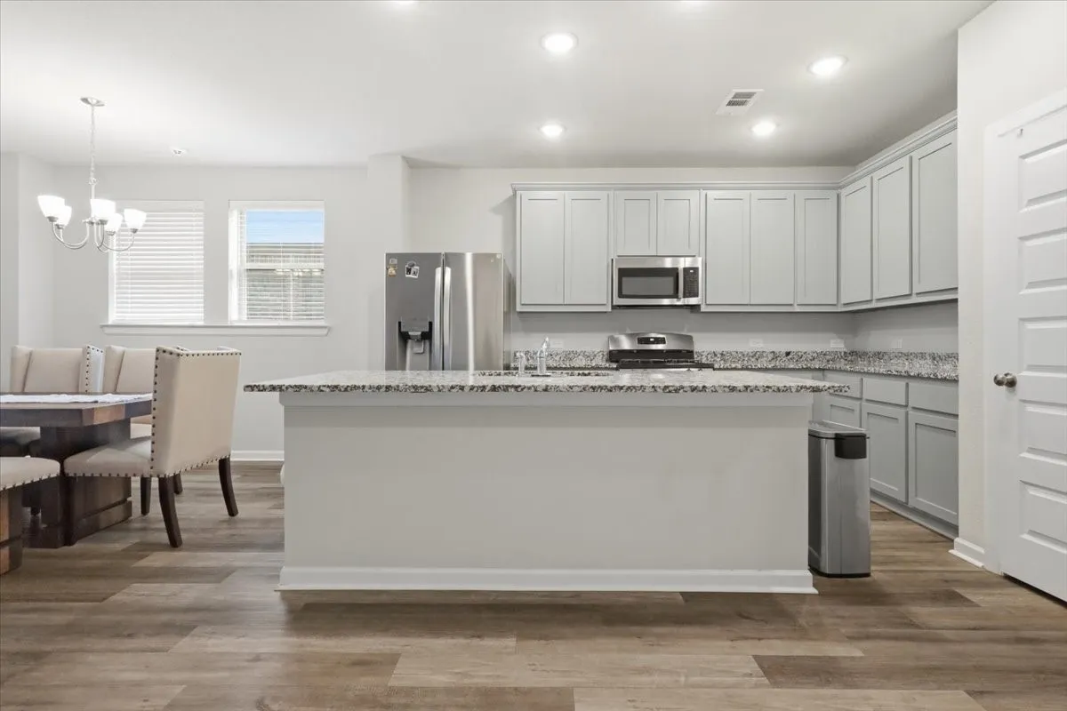Open-concept kitchen and dining area featuring wood-finish flooring, recessed lighting, light gray cabinetry, and stainless steel appliances