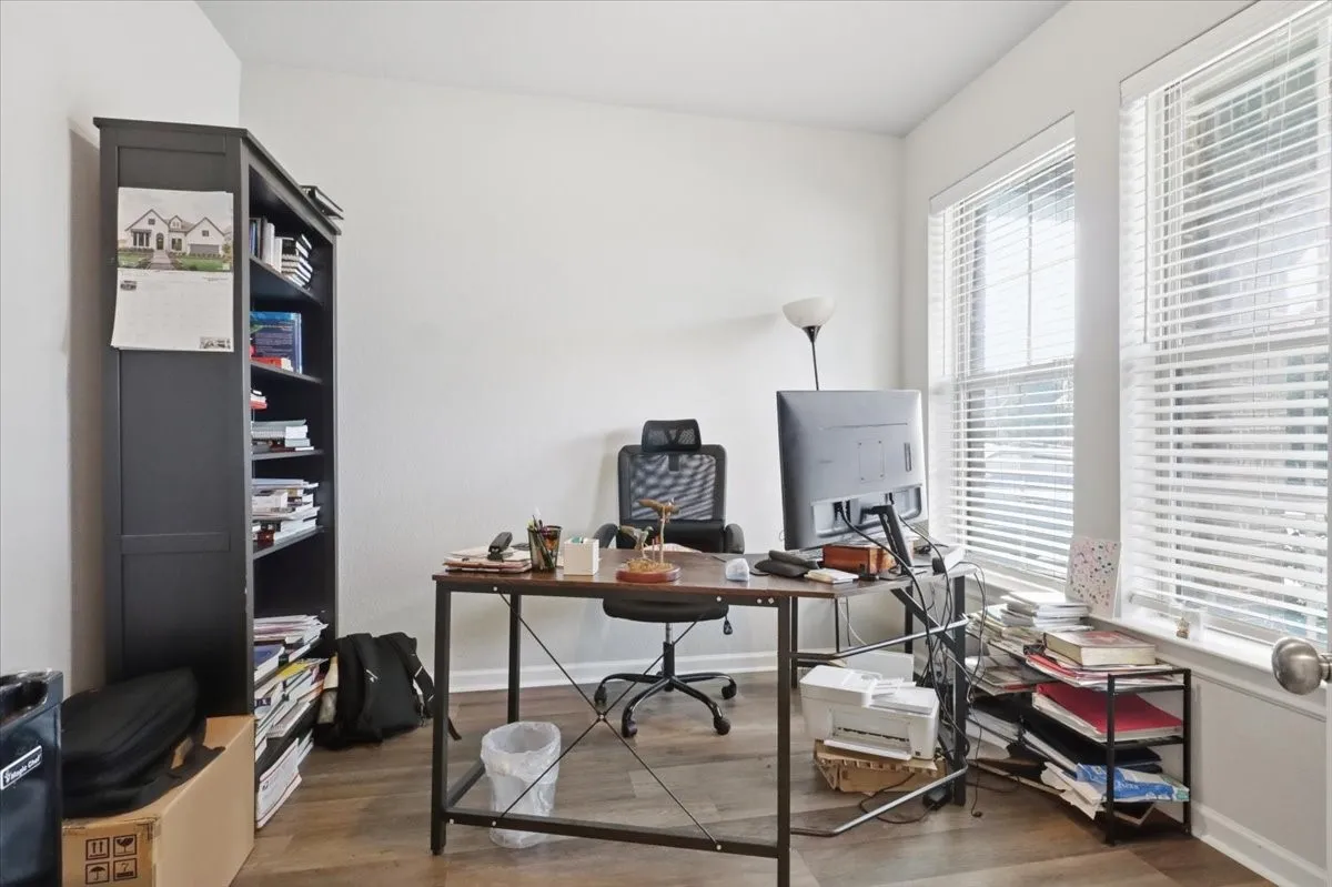 Room with wood-finish flooring, white walls, and multiple windows with blinds