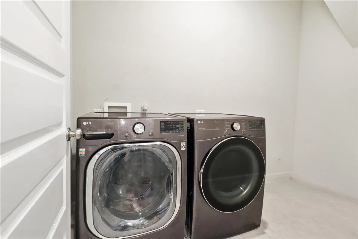 Dedicated laundry area featuring a front-loading washer and dryer set, white paneled door, and light-toned flooring