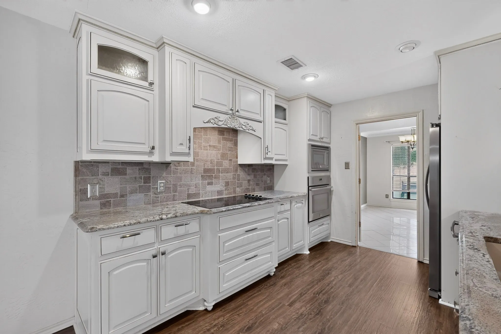 Kitchen featuring light-toned cabinetry, granite countertops, tile backsplash, and wood-finish flooring