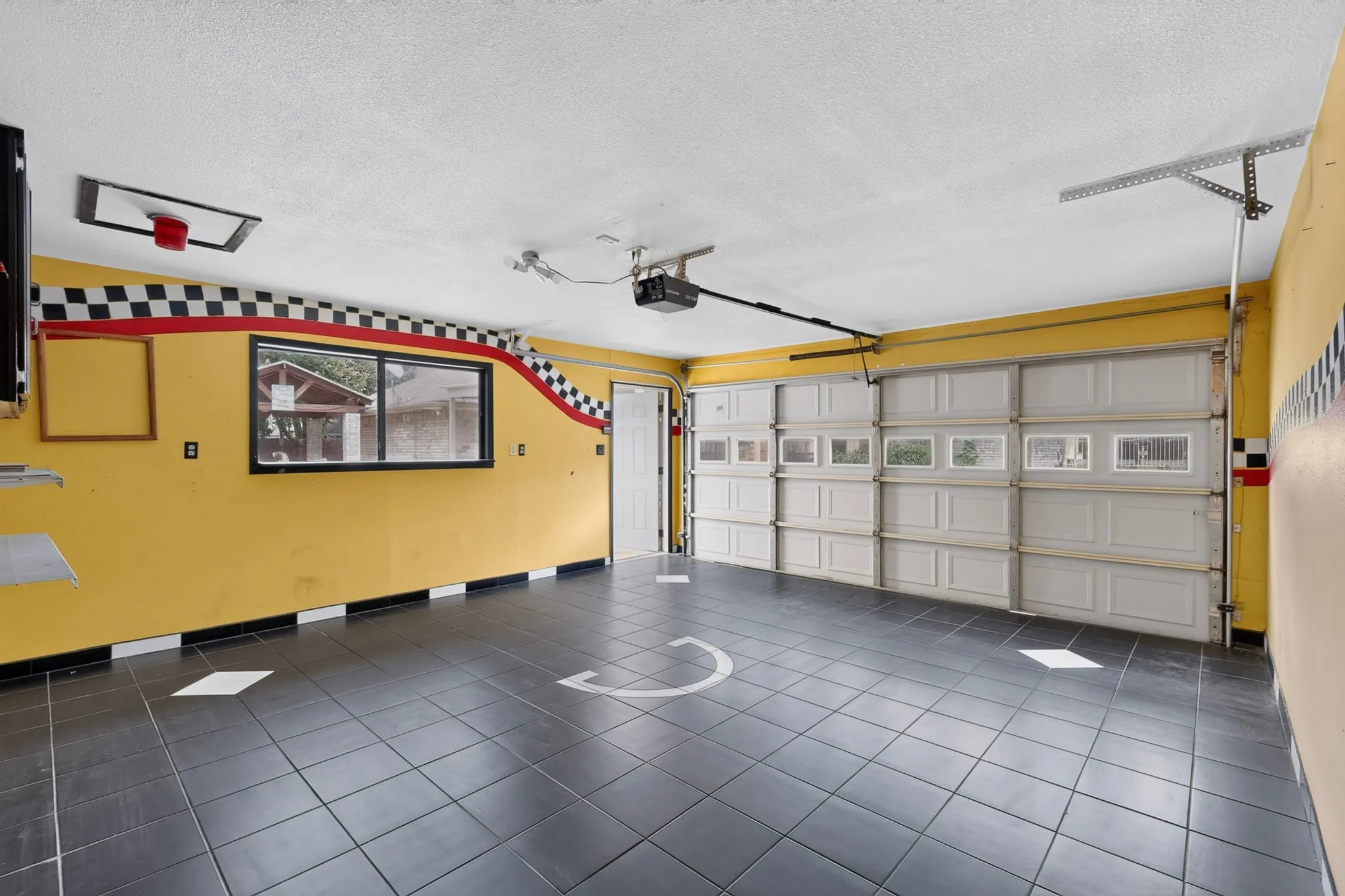 Spacious garage featuring dark tile flooring, a large overhead door with window inserts, and a side access door