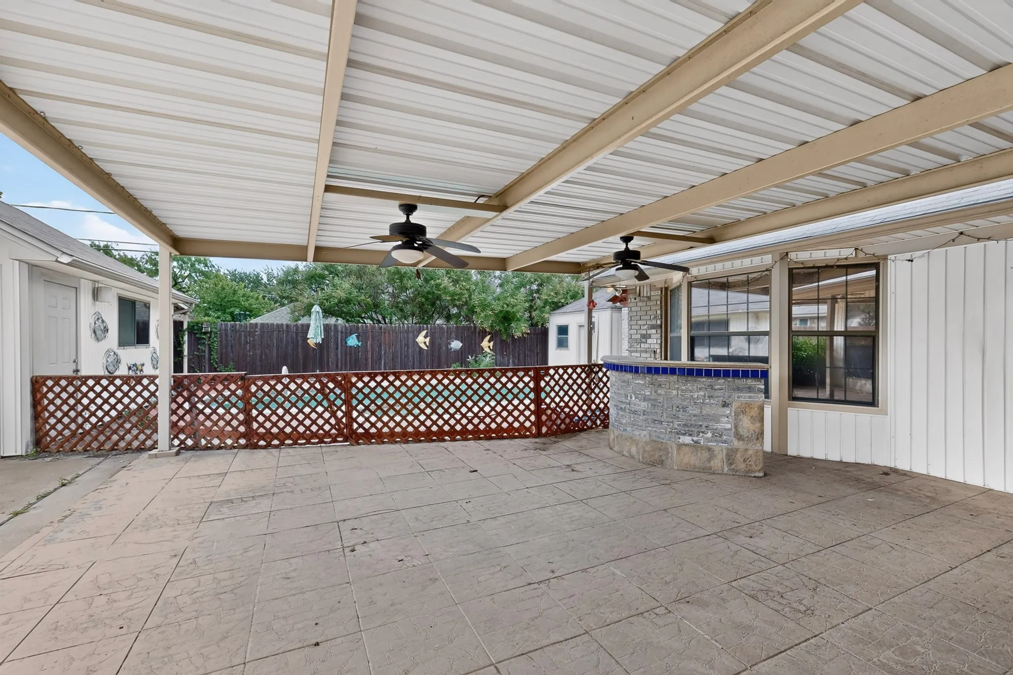Expansive covered patio featuring a stamped concrete surface, ceiling fans, and a stone-clad wet bar with a tiled countertop