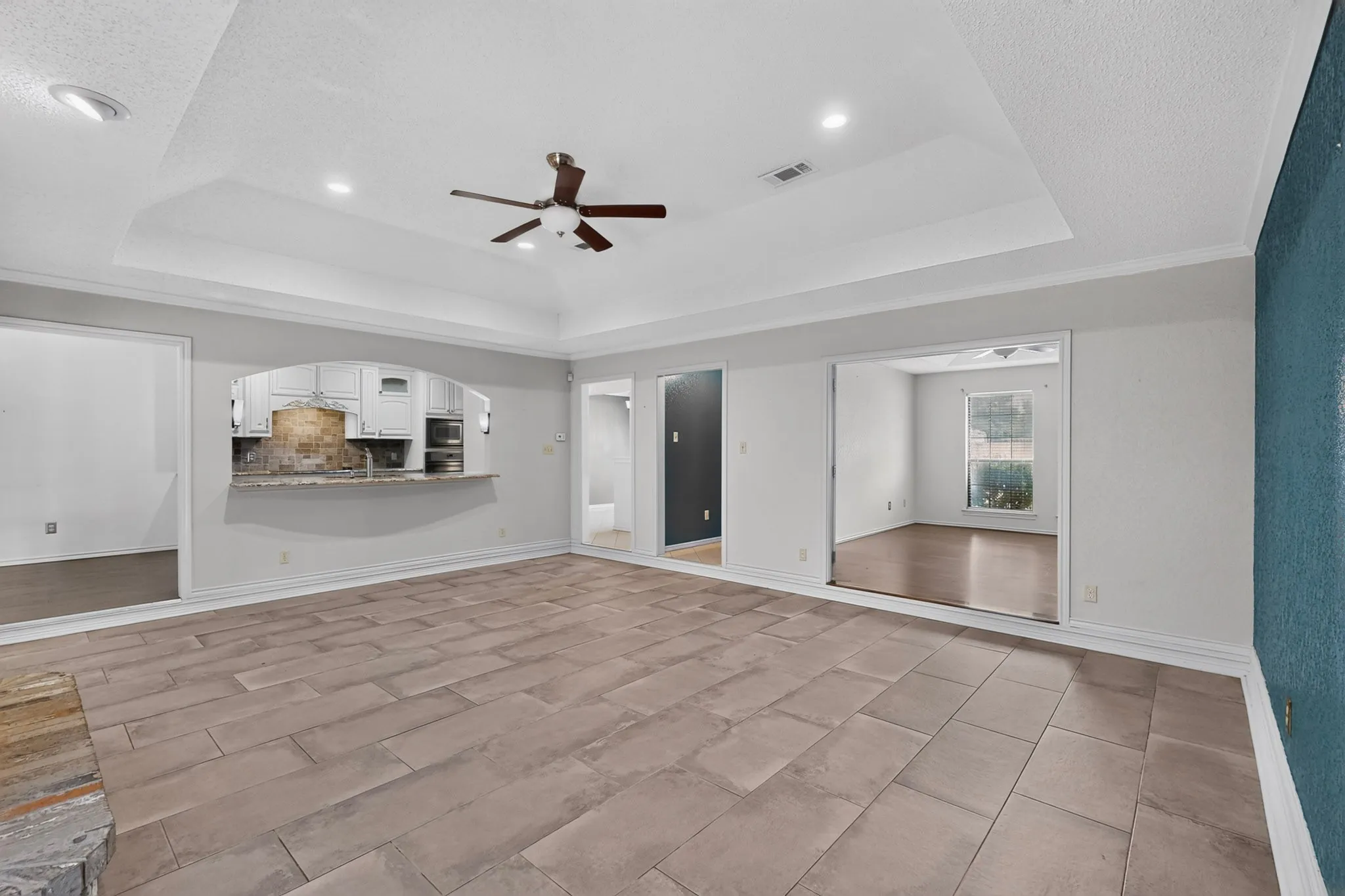 Spacious living area featuring large format tile flooring, a tray ceiling with recessed lighting, and a ceiling fan