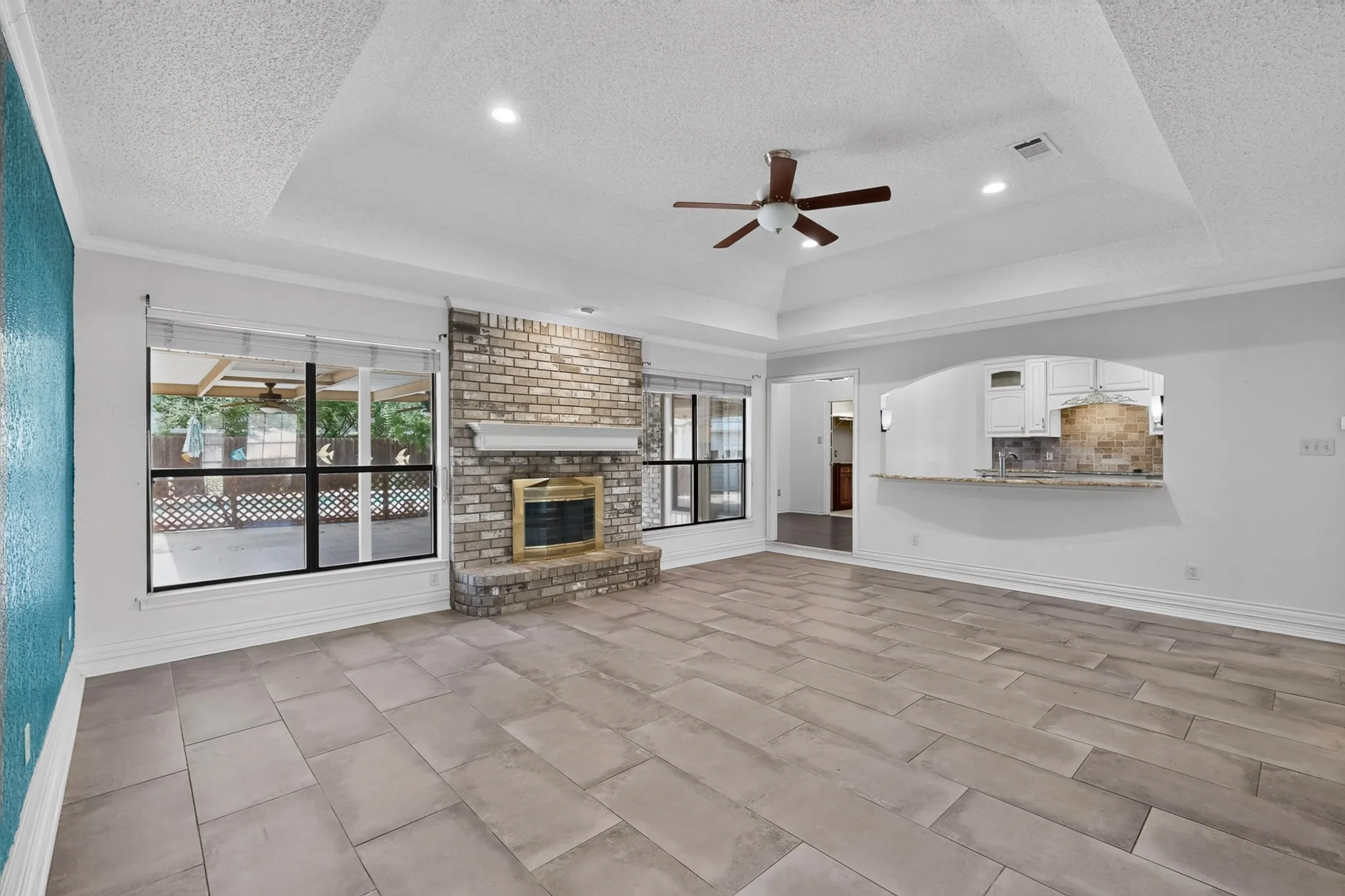 Spacious living area featuring wood-finish tile flooring, a brick fireplace with a white mantel, and large windows