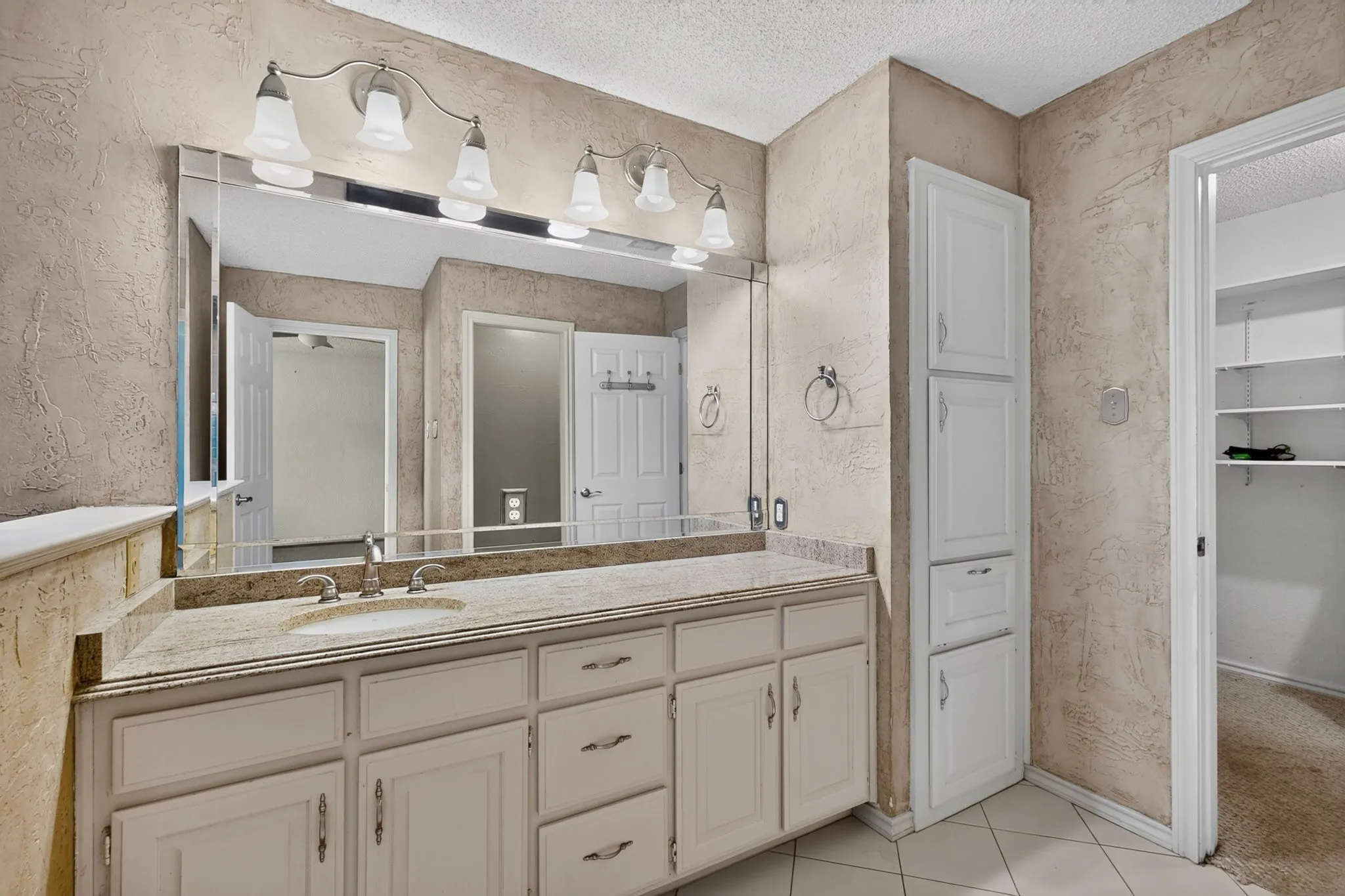 Bathroom featuring a single vanity with an integrated sink, a large wall-mounted mirror, and a multi-bulb vanity light fixture