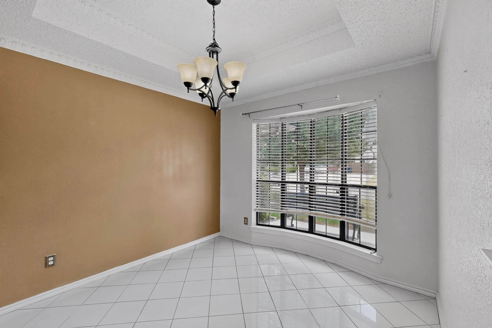 Bay window with horizontal blinds, overhead chandelier, white tile flooring, tray ceiling, and crown molding