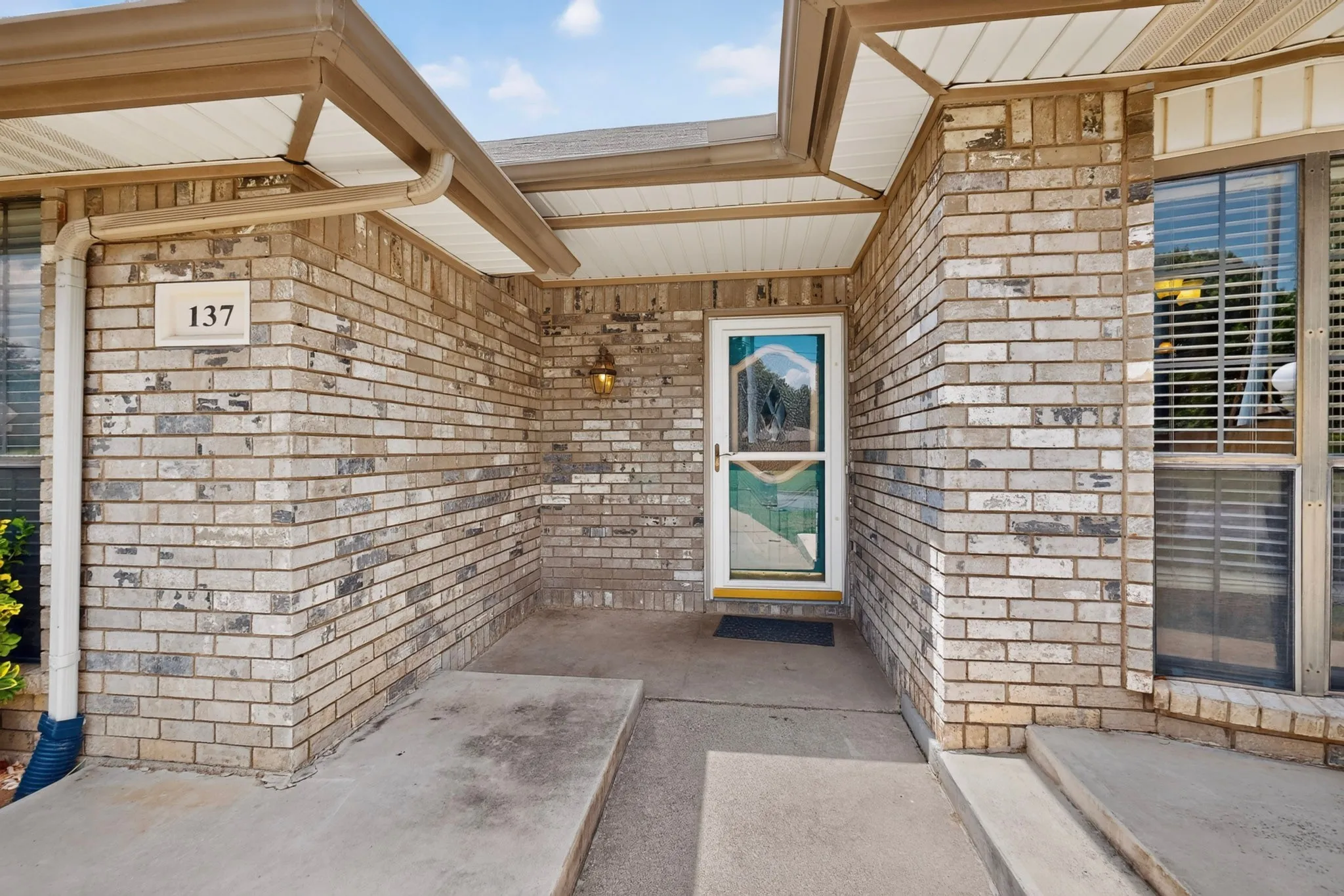 Brick exterior featuring a covered entry, glass-paneled storm door, and decorative outdoor lighting