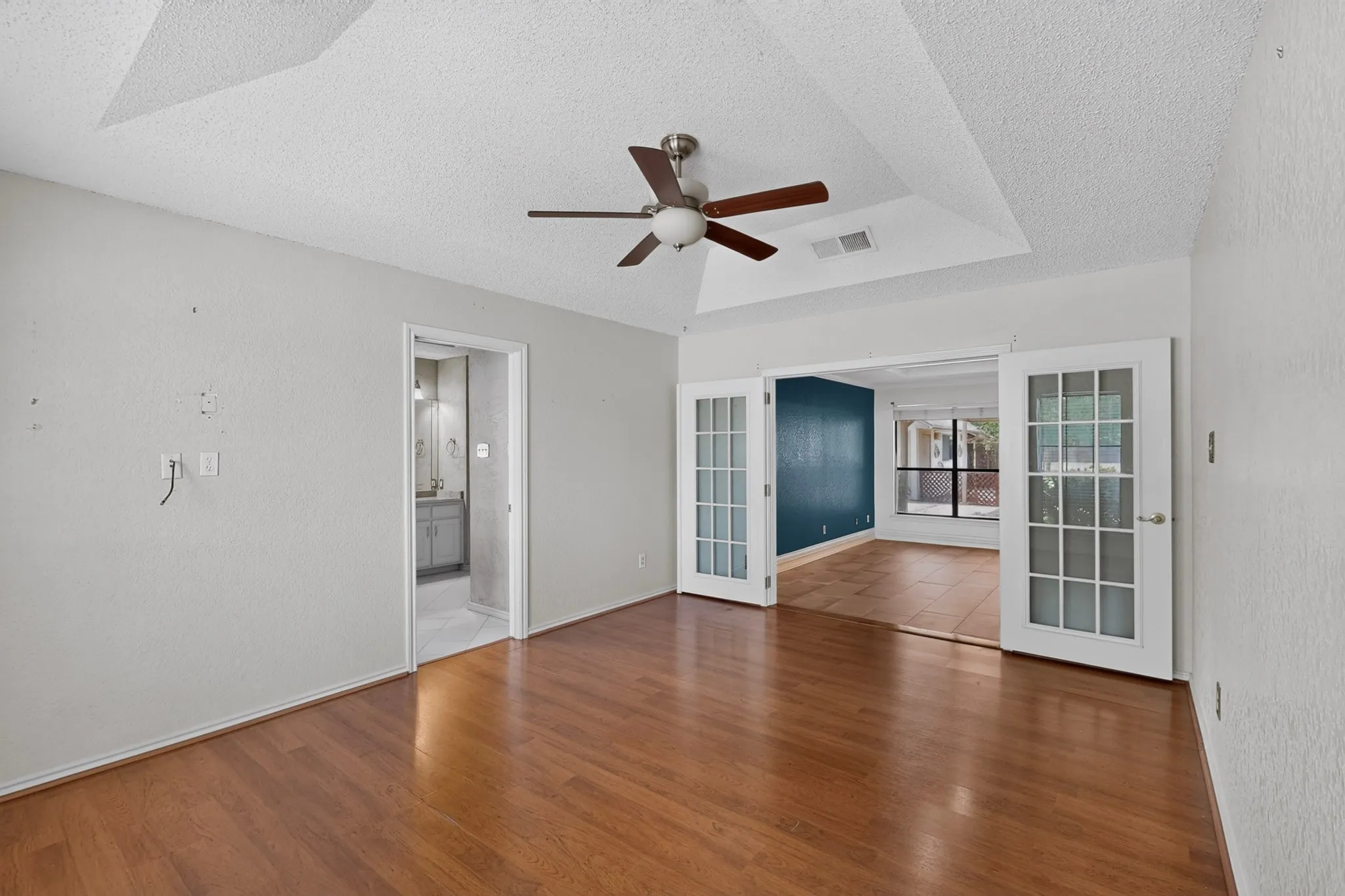 Spacious room featuring wood-finish flooring, a tray ceiling, and a ceiling fan