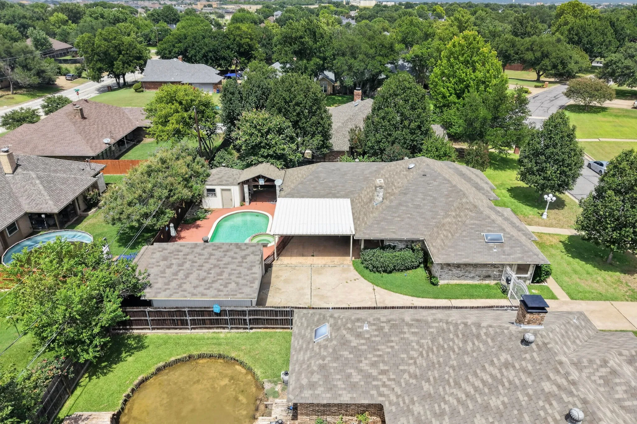 Spacious property featuring a large in-ground swimming pool, an expansive paved patio area, and mature trees providing ample shade