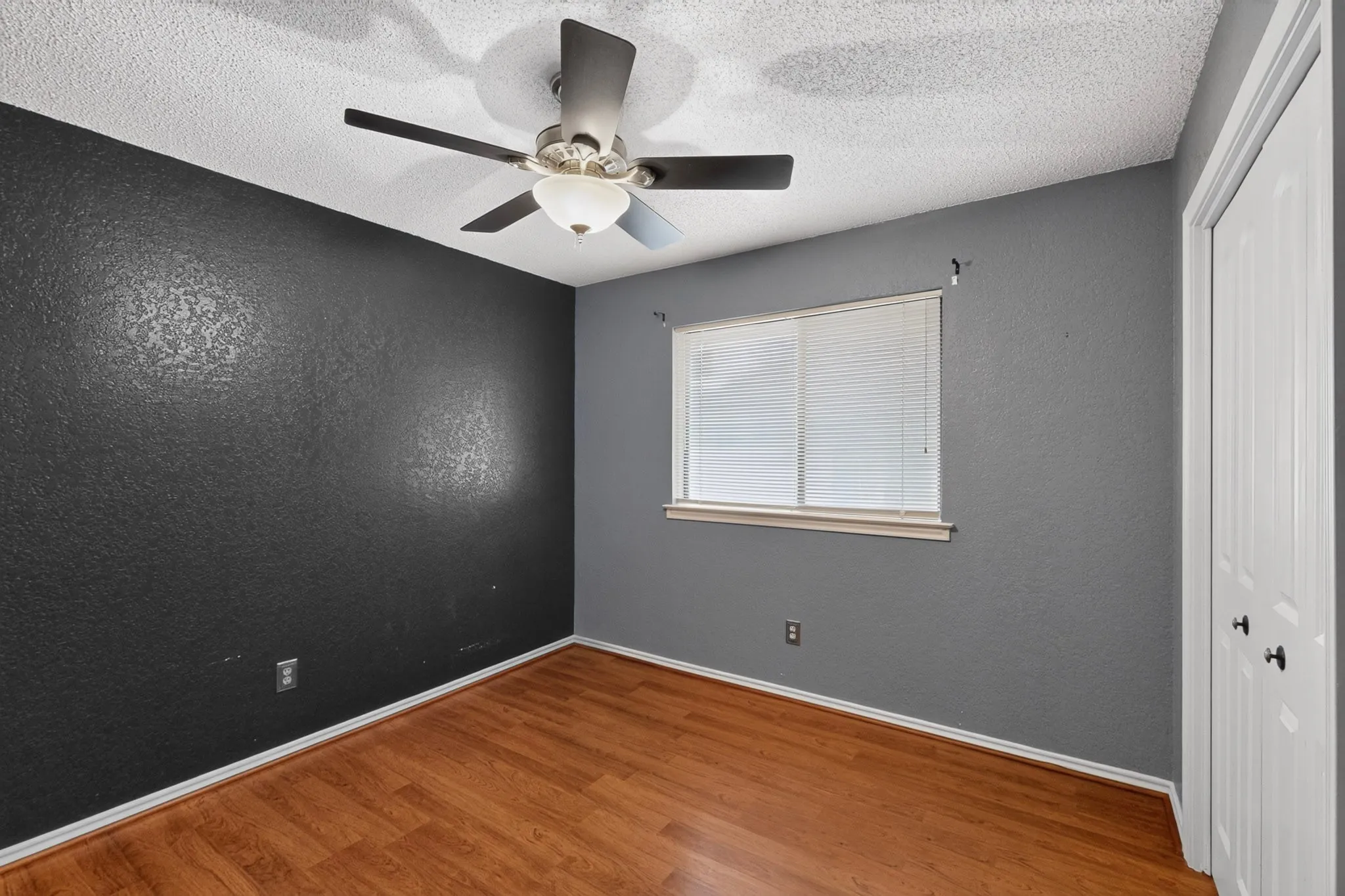 Room featuring wood-finish flooring, a ceiling fan with integrated lighting, and a window with blinds