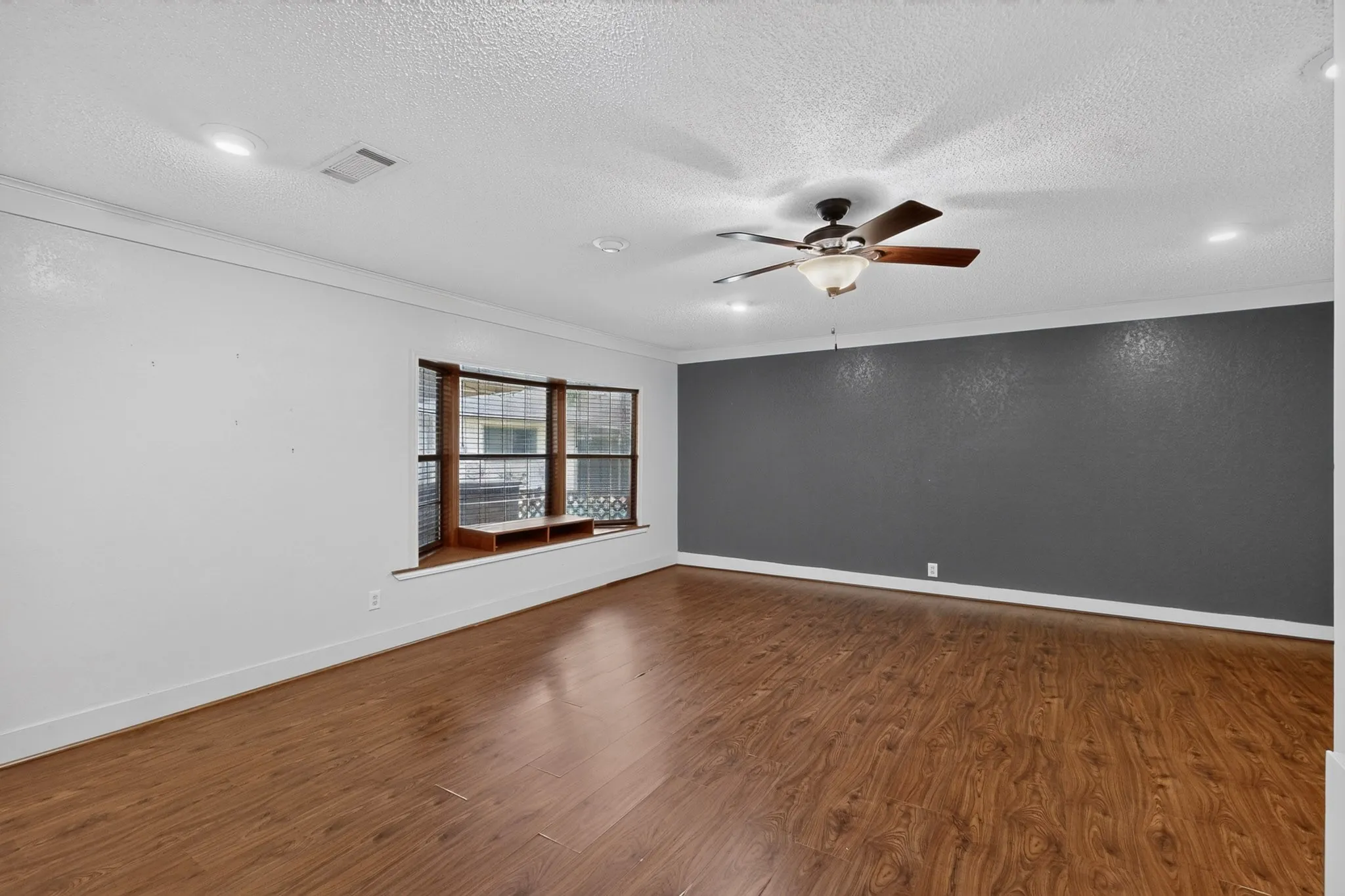 Spacious room featuring rich wood-finish flooring, a prominent accent wall, and a multi-pane bay window with a built-in window seat