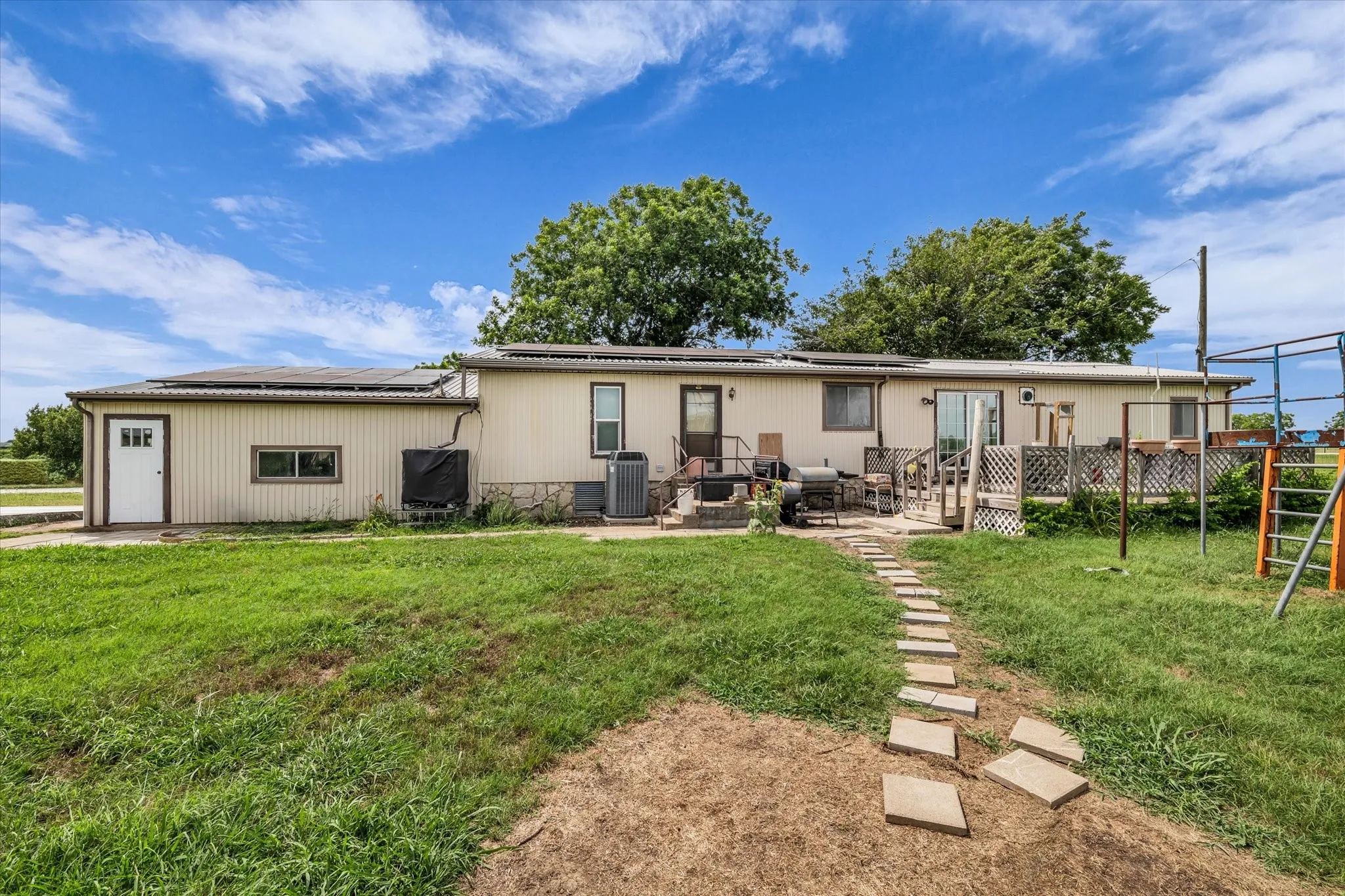 Expansive backyard with a stone paver pathway, a raised wood deck, and a concrete patio