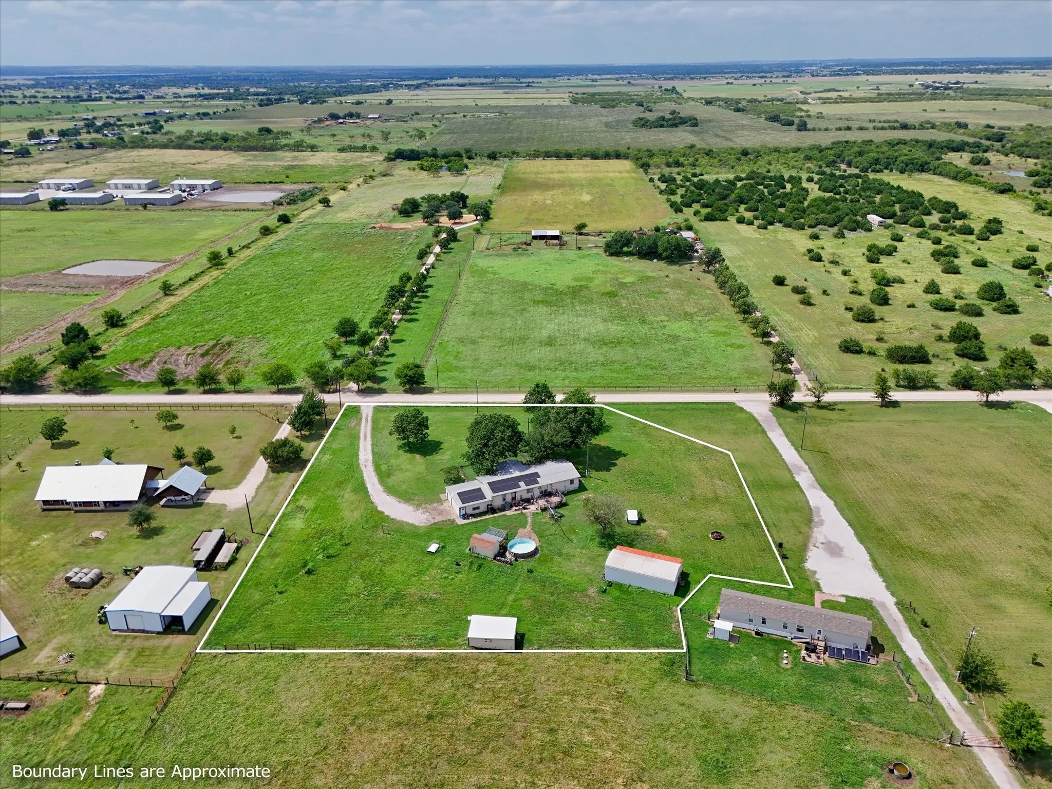 Expansive rural property featuring multiple structures, verdant green space, a long driveway, and mature trees