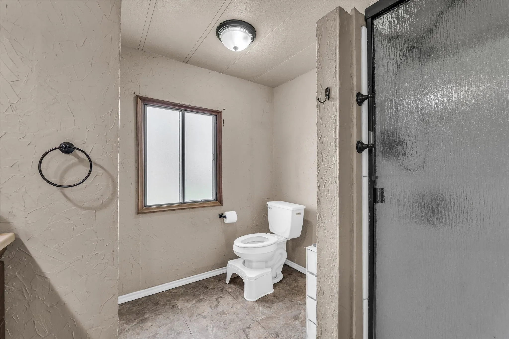 Bathroom featuring a frosted window, textured wall finish, and a shower with a dark-framed frosted glass door