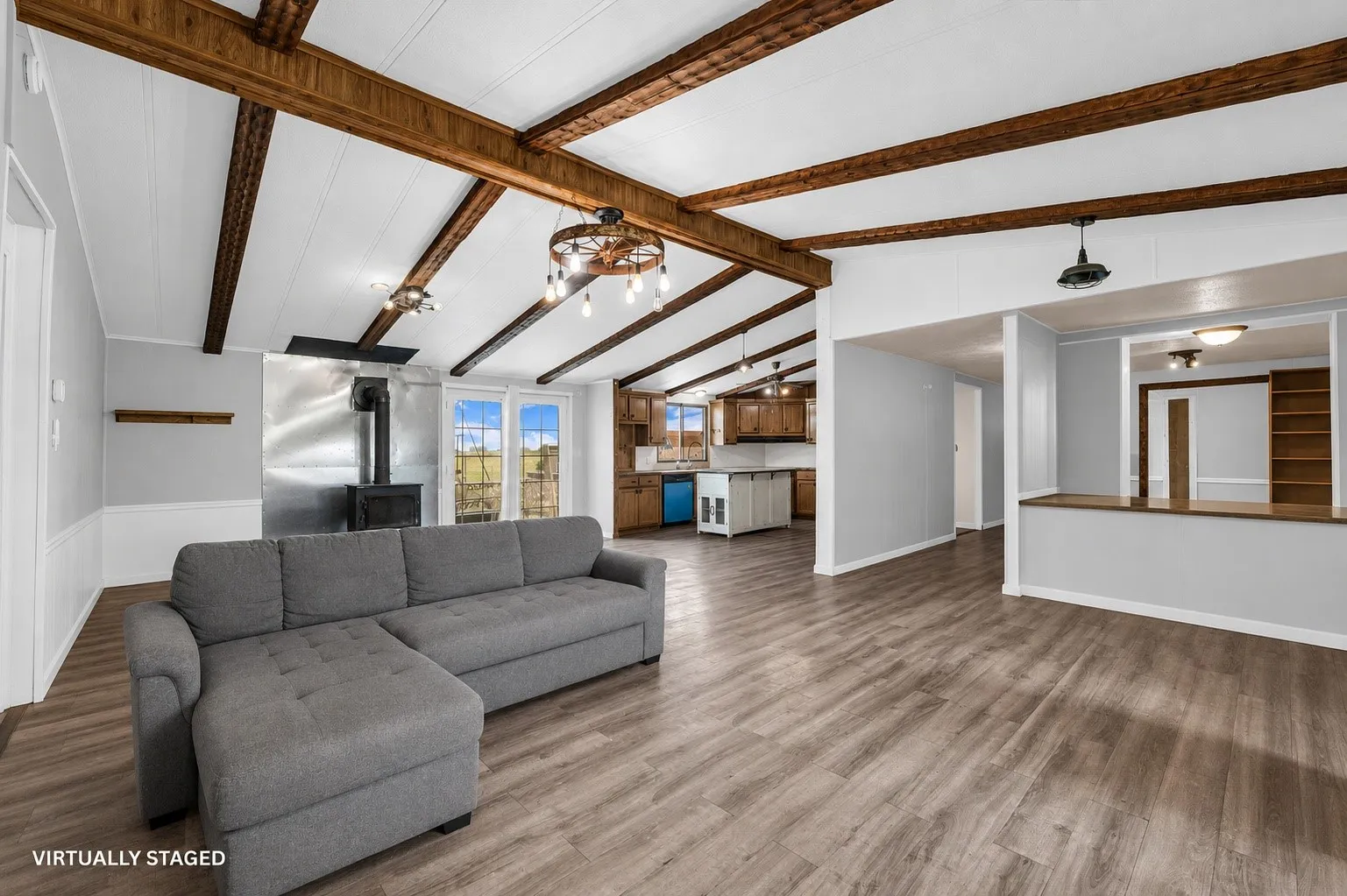 Open-concept living space with exposed wood beams, wood-finish flooring, and a wood-burning stove.