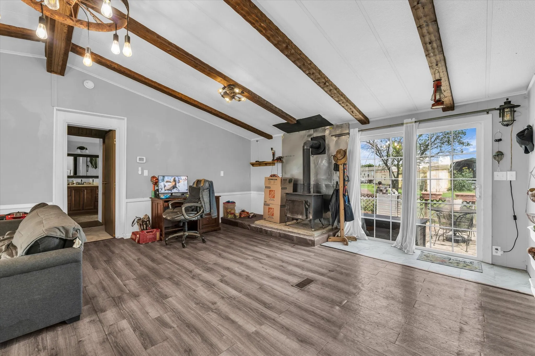 Vaulted ceiling with exposed wood beams, wood-finish flooring, wood-burning stove with stone hearth, and sliding glass doors to outdoor patio