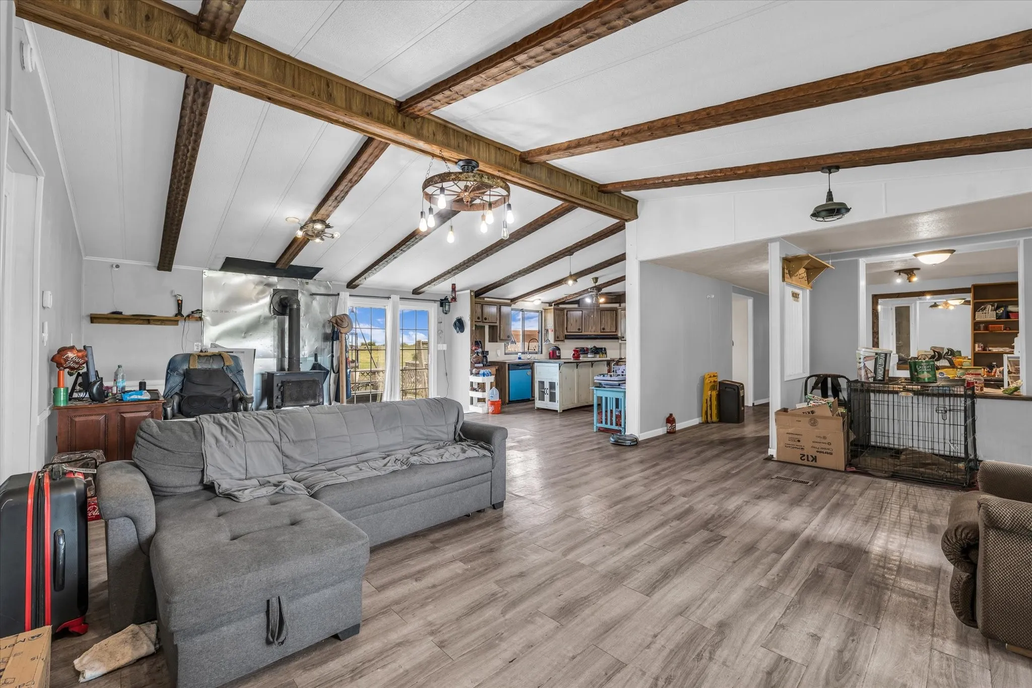 Vaulted ceilings with exposed wood beams, wood-finish flooring, wood-burning stove, pendant lighting, and double French doors