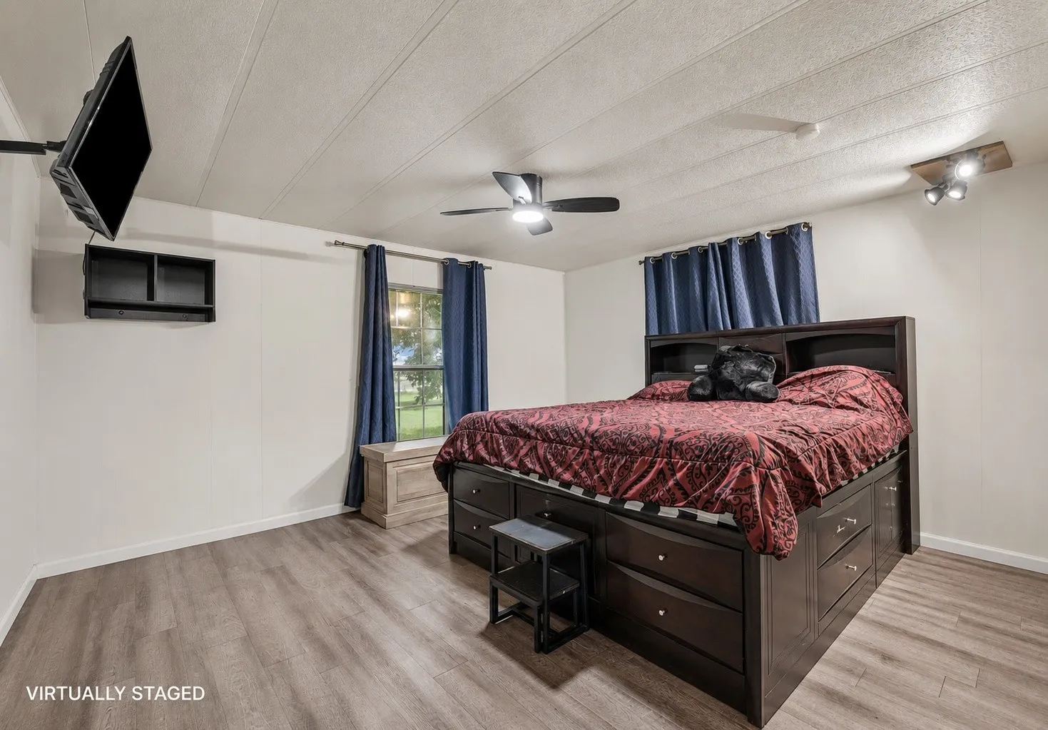 Spacious room featuring wood-finish flooring, white walls, and a ceiling fan