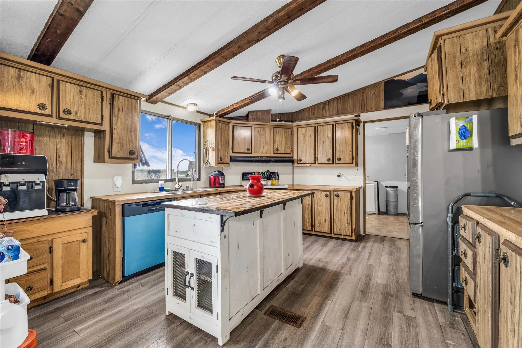Kitchen featuring wood-finish cabinetry, a central island with a wood-finish countertop, wood-finish flooring, a ceiling fan, and exposed wood beams