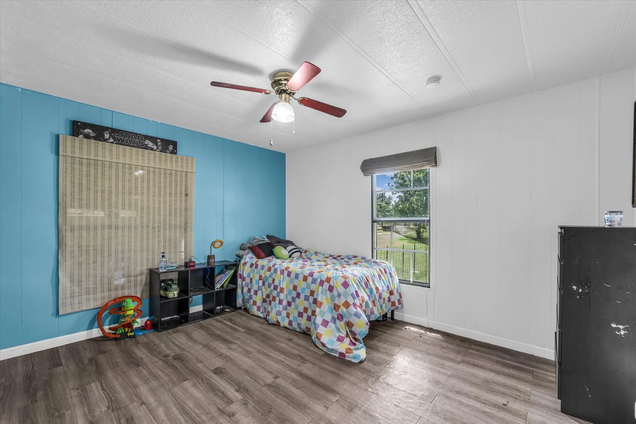 Wood-finish flooring, ceiling fan with light fixture, and window with exterior landscaping