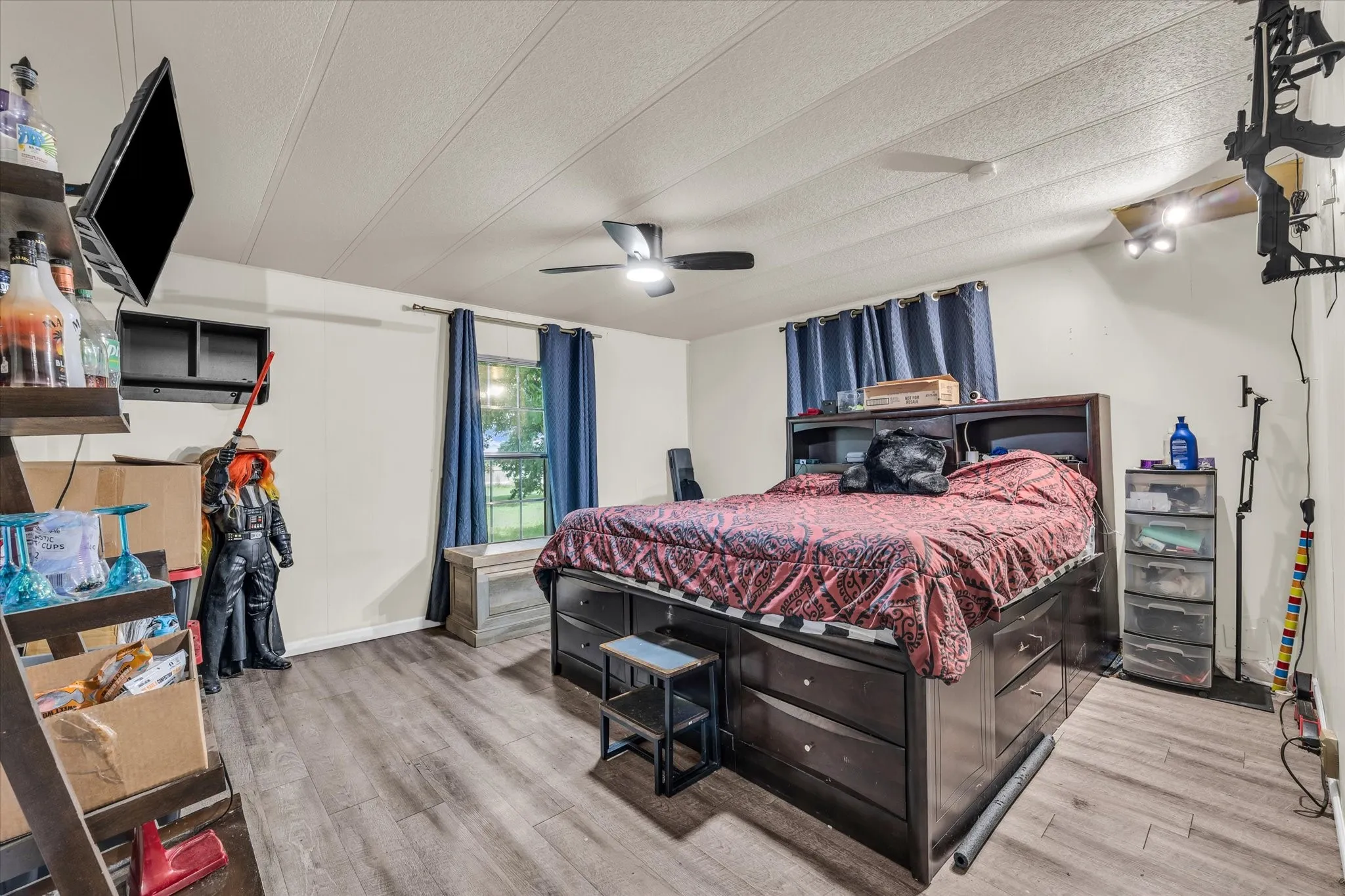 Spacious bedroom featuring wood-finish flooring, built-in storage with multiple drawers, blue window treatments, and ceiling fan