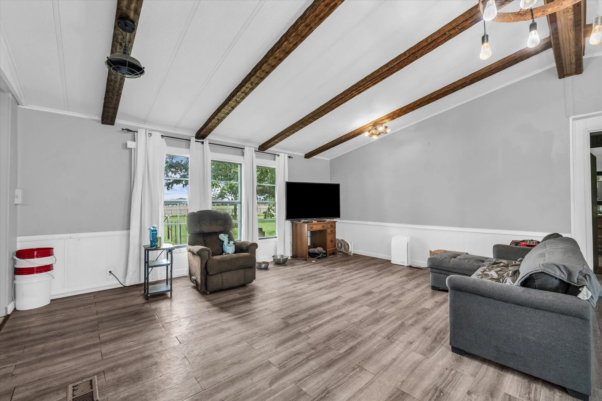 Vaulted ceiling with exposed wood beams, wood-finish flooring, white wainscoting, and multiple windows