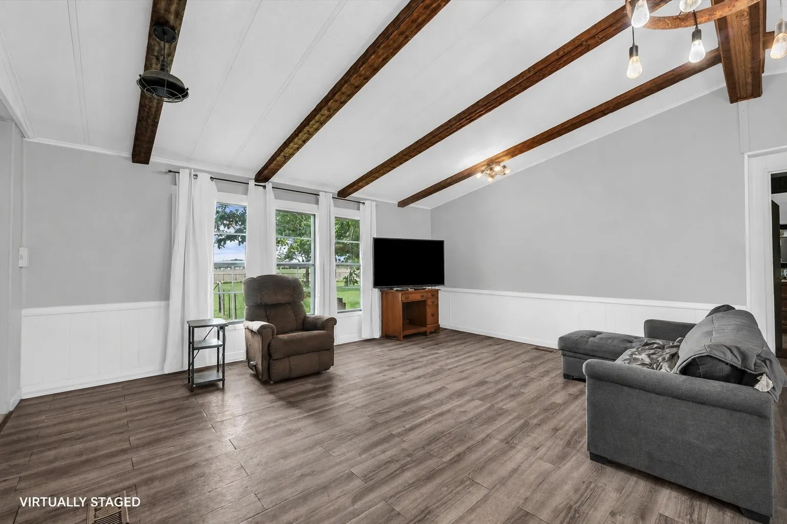 Spacious living area featuring a vaulted ceiling with exposed wood beams, wood-finish flooring, and multiple windows