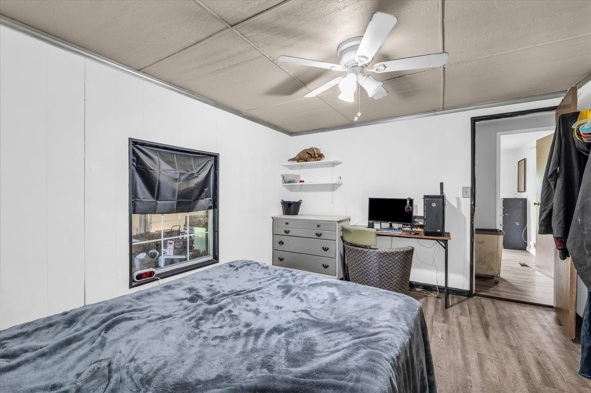 Wood-finish flooring, ceiling fan with integrated lighting, wall-mounted shelving, and a paneled ceiling
