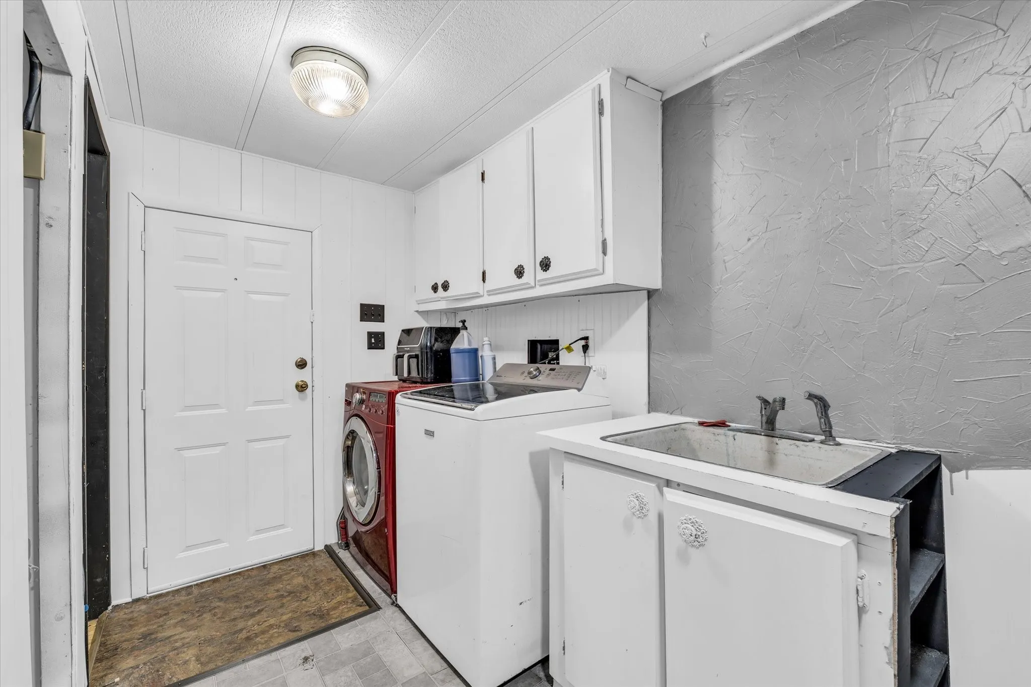 Laundry area featuring white paneled walls, a utility sink with base cabinetry, upper white storage cabinets, and a durable flooring surface