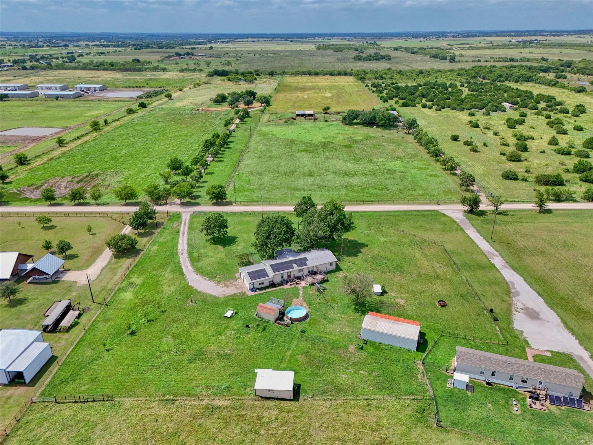 Expansive rural property featuring multiple structures, verdant green space, a long driveway, and mature trees