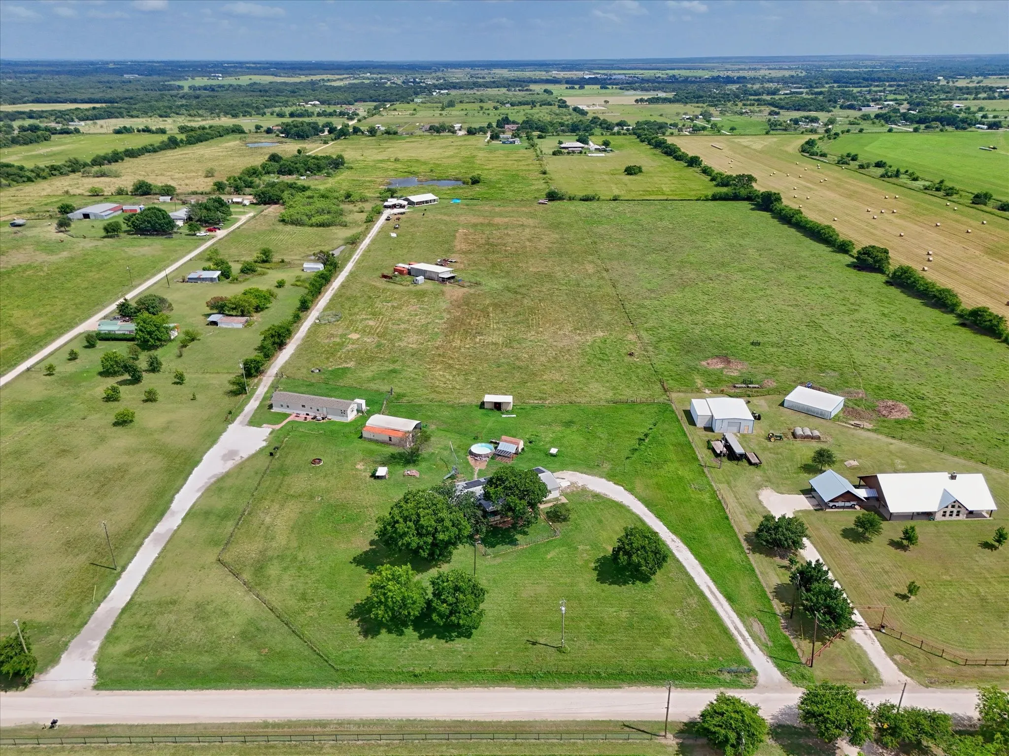 Expansive rural property featuring multiple structures, verdant green space, a long driveway, and mature trees