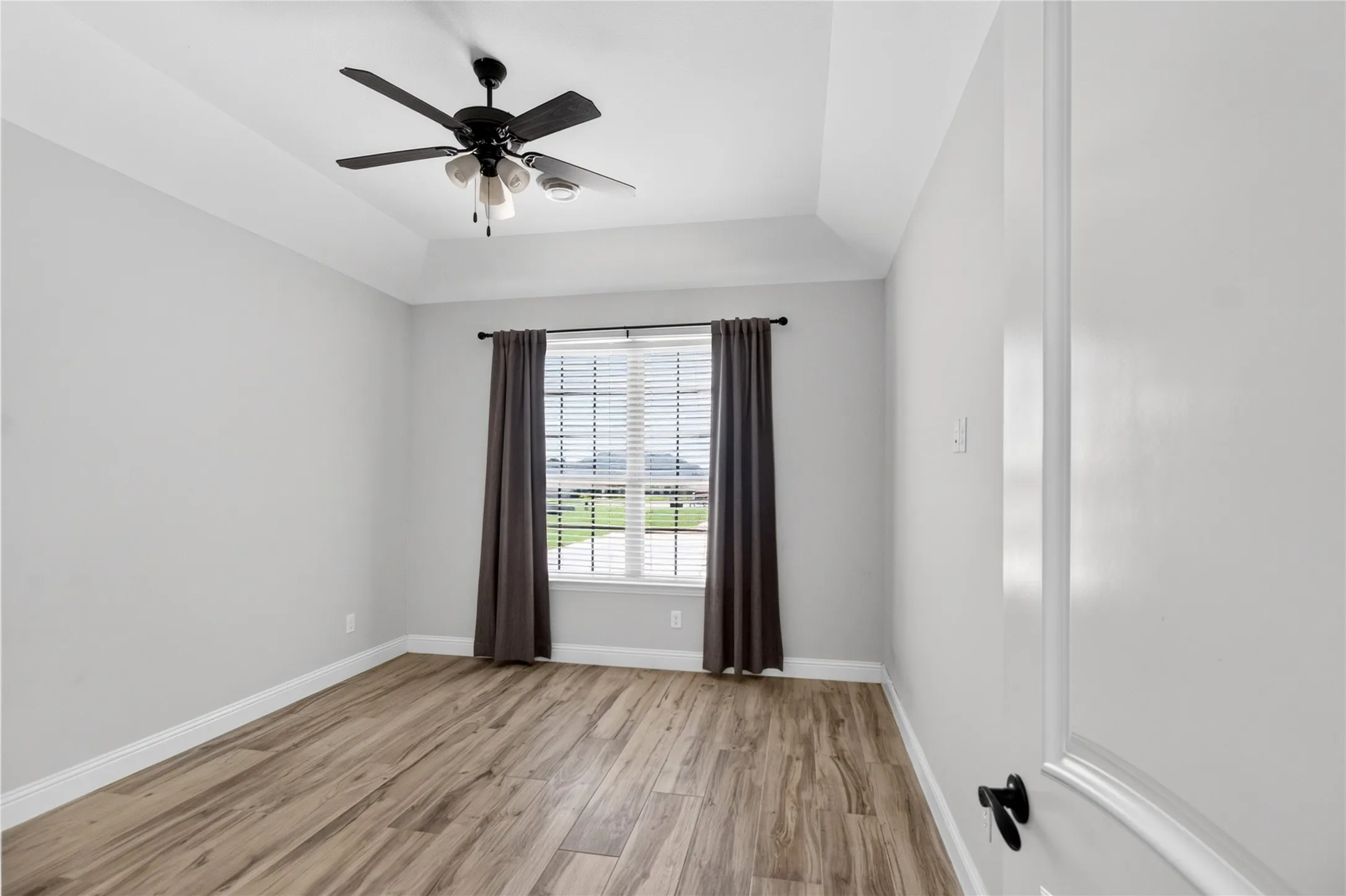 Interior room featuring wood-finish flooring, a tray ceiling, and a ceiling fan with integrated lighting