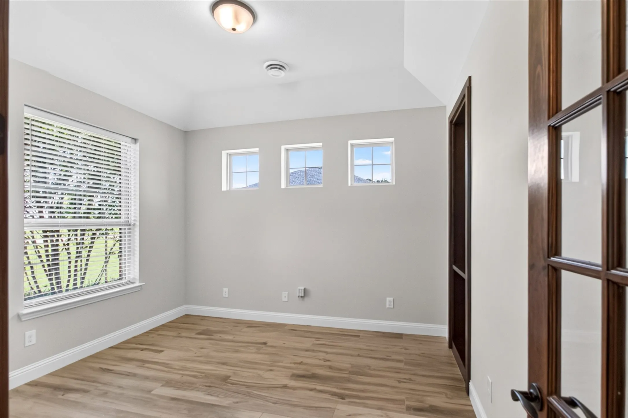 Spacious room with wood-finish flooring, light grey walls, and a recessed ceiling