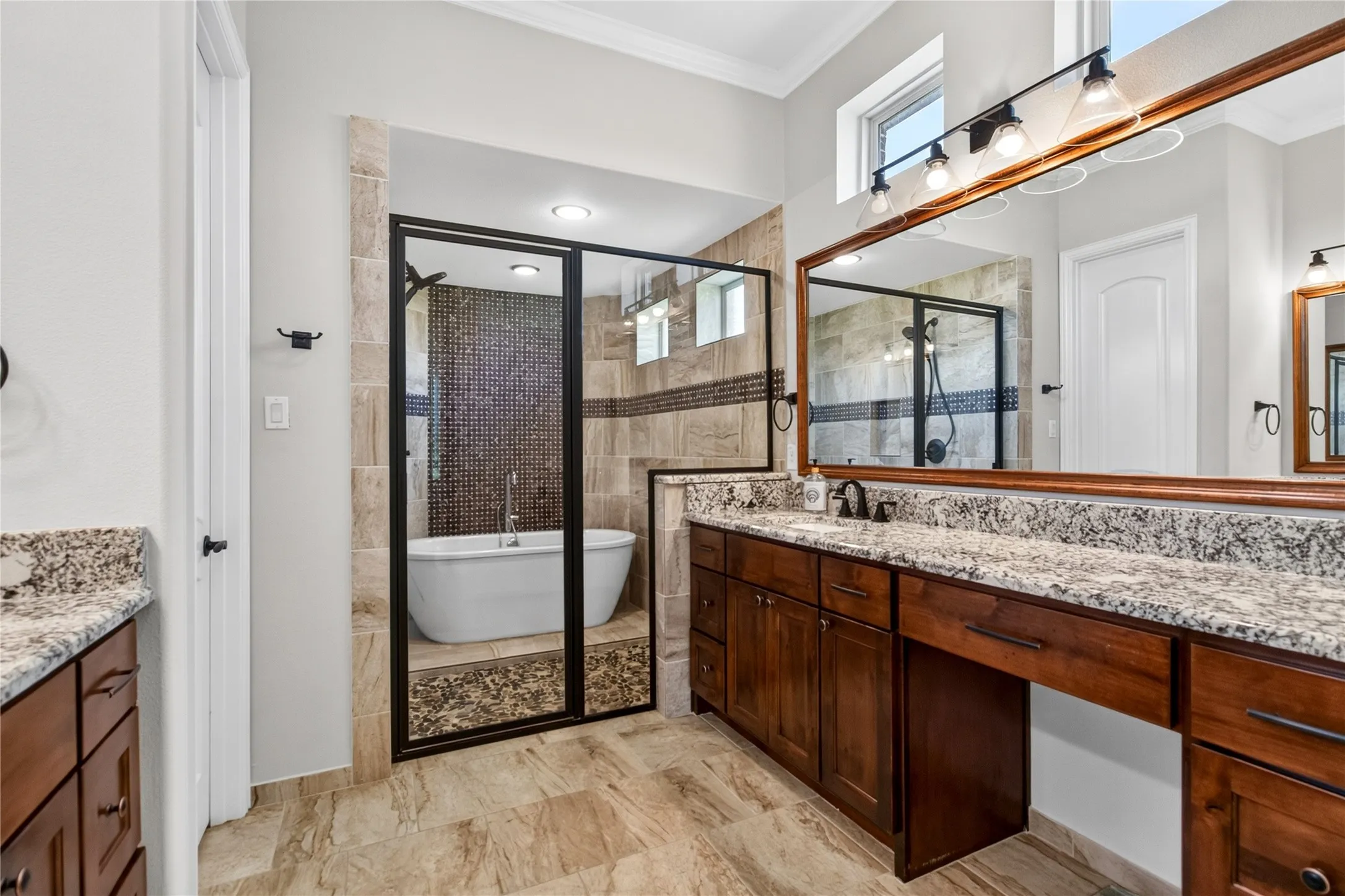 Bathroom featuring a freestanding tub within a glass-enclosed shower, dual vanities with stone countertops, wood cabinetry, and tiled flooring