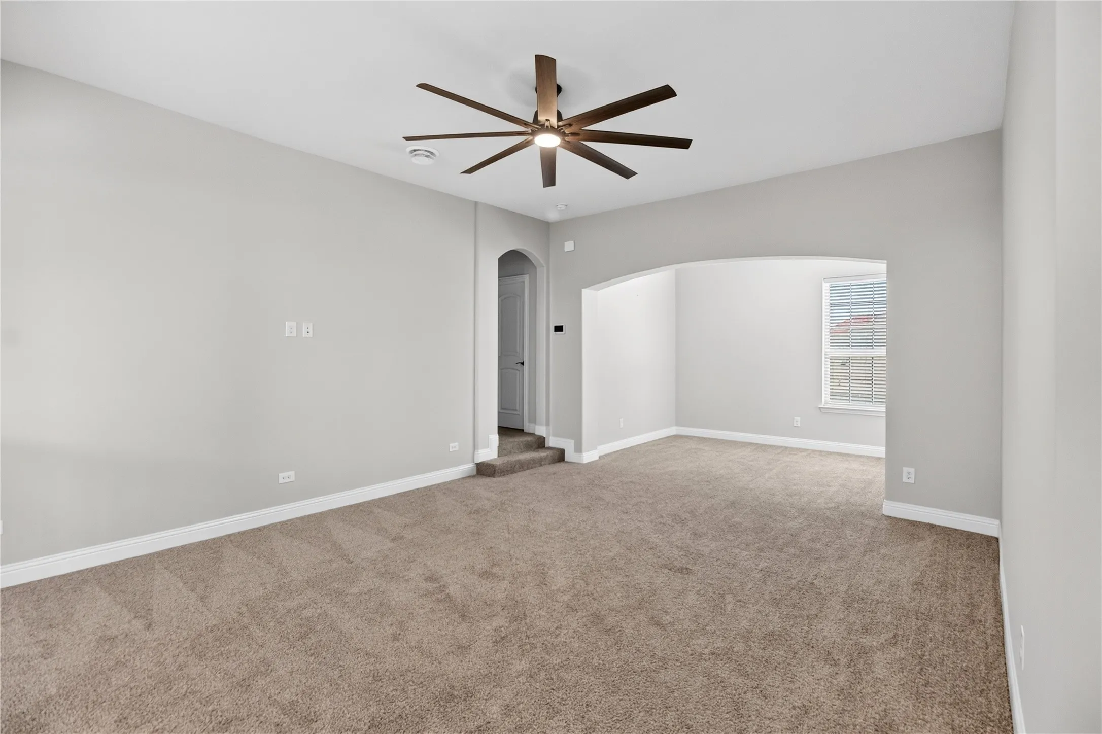 Spacious room featuring neutral carpeting, light gray wall paint, and a multi-blade ceiling fan