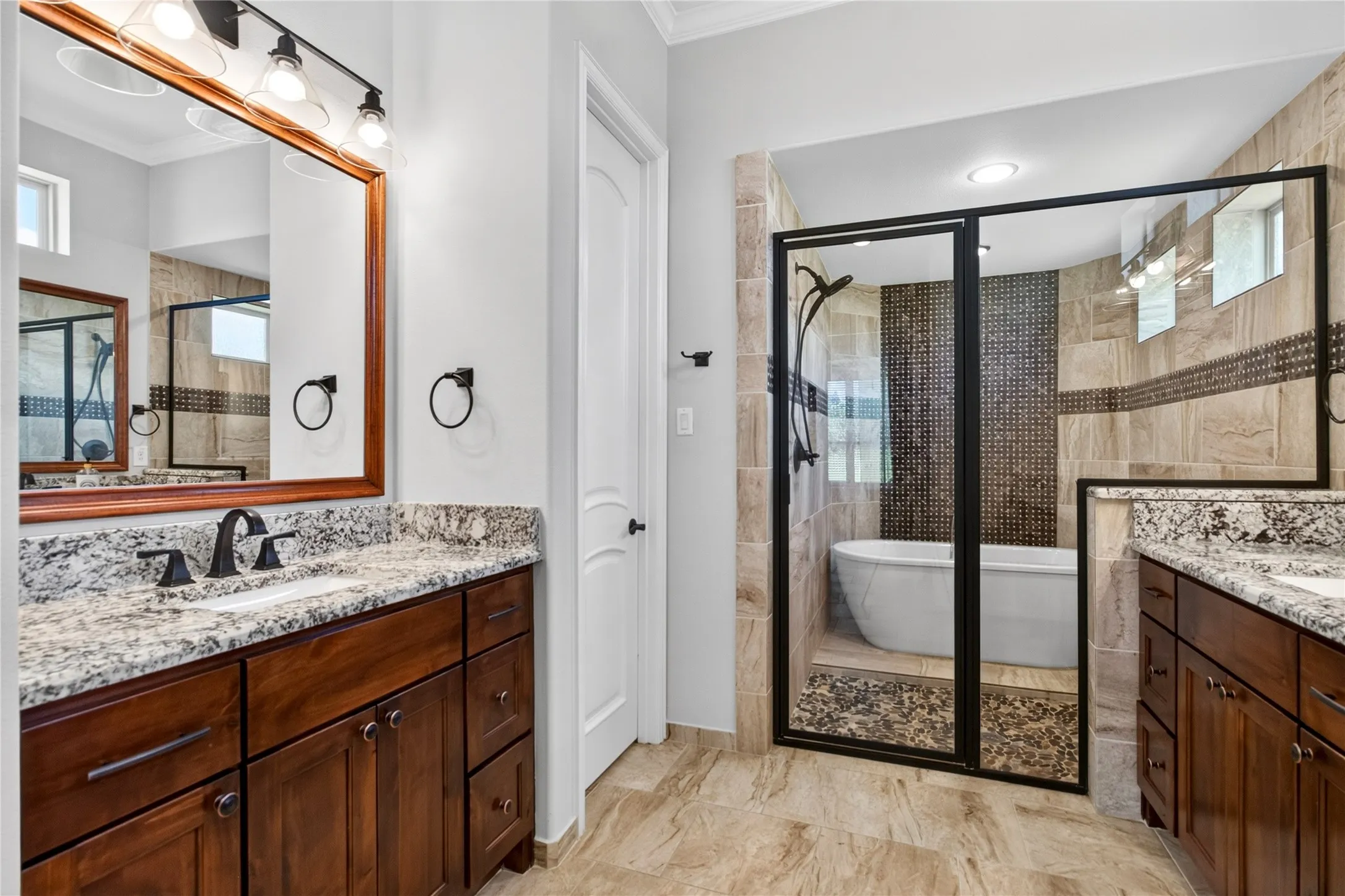 Bathroom featuring a freestanding tub within a glass-enclosed shower, dual vanity with granite countertops, wood-finish cabinetry, and tiled flooring