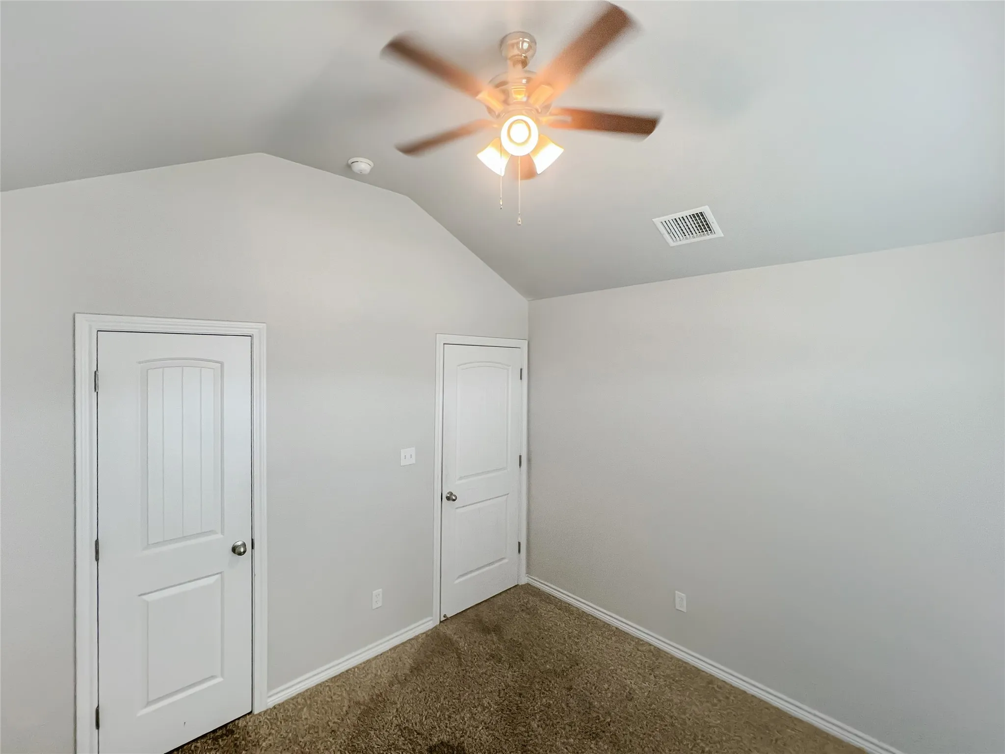 Vaulted ceiling with a ceiling fan light fixture, two panel doors, and neutral wall tones