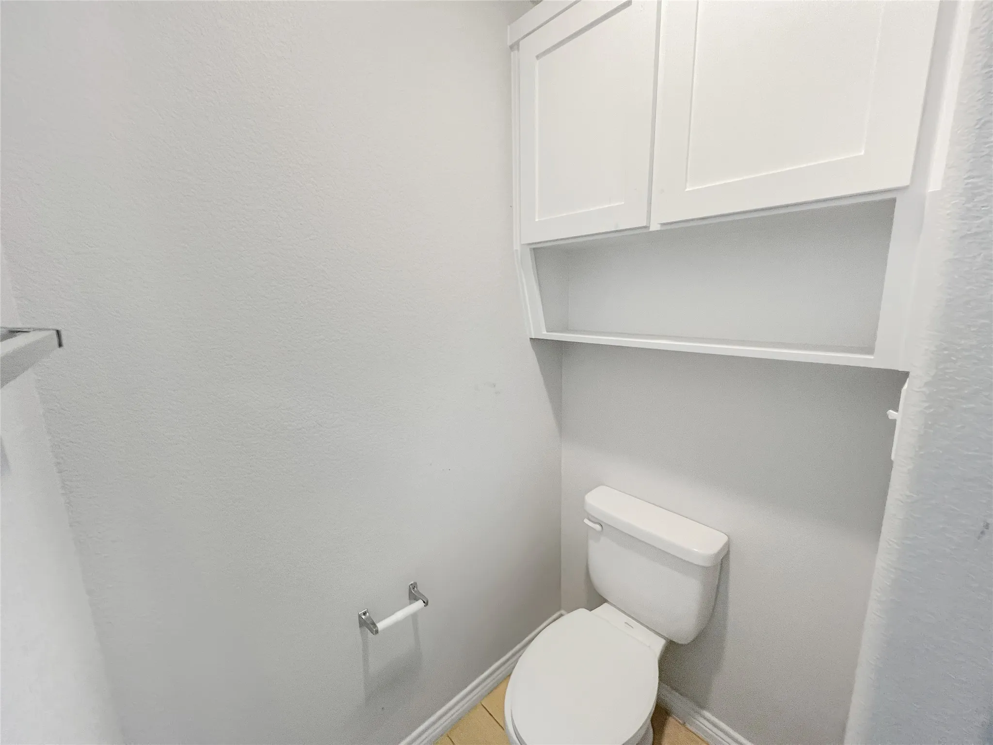White toilet with built-in overhead cabinetry featuring two shaker-style doors and an open shelf