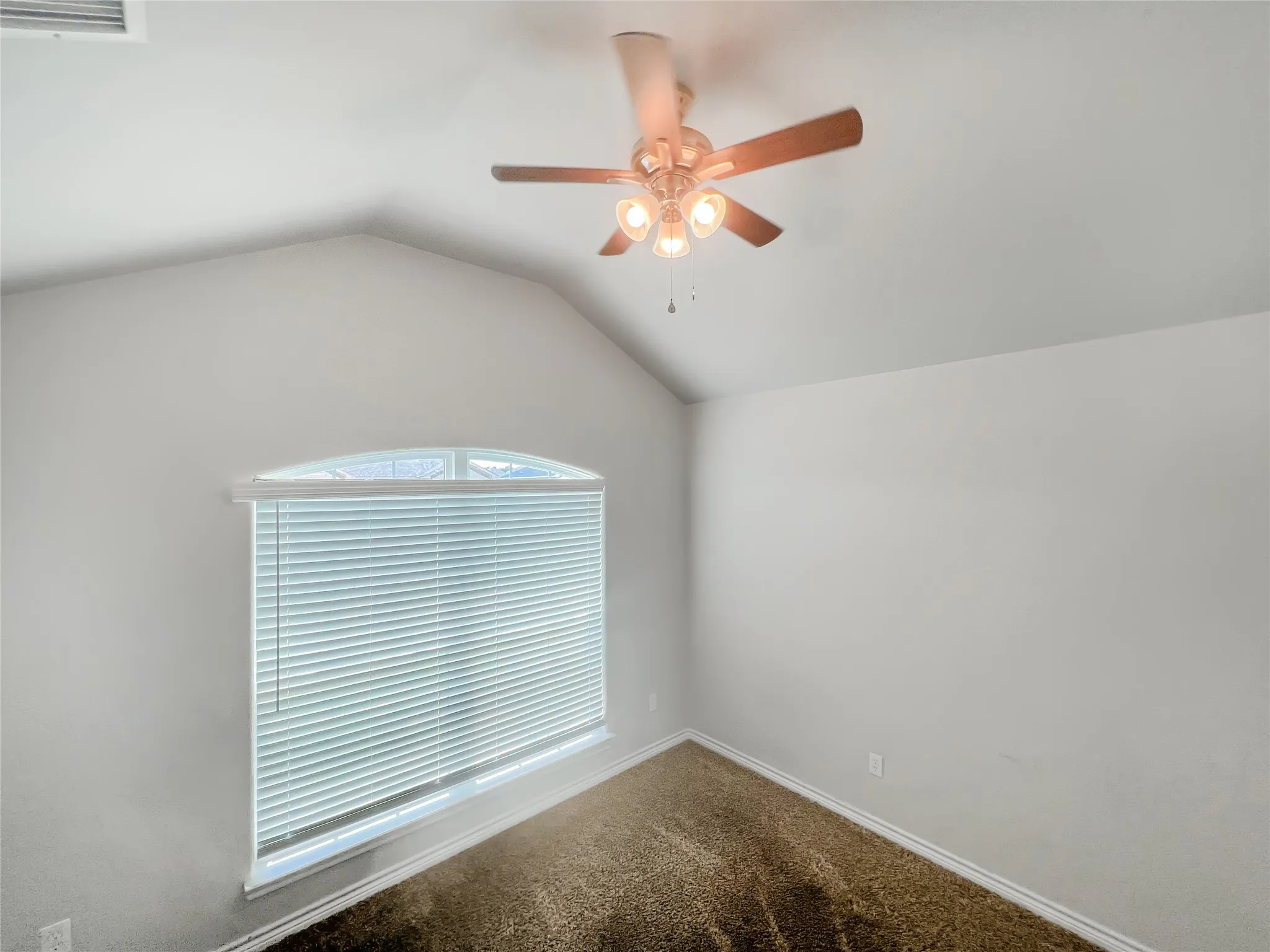 Room featuring vaulted ceilings, a ceiling fan with light fixture, window with arched transom, horizontal blinds, and carpet flooring