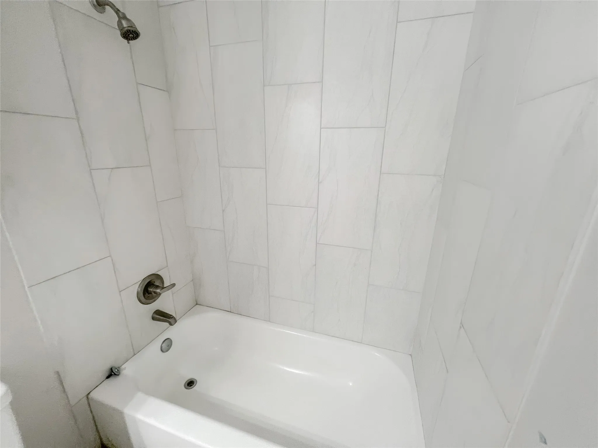 White bathtub with an integrated shower, surrounded by light-toned rectangular wall tiles