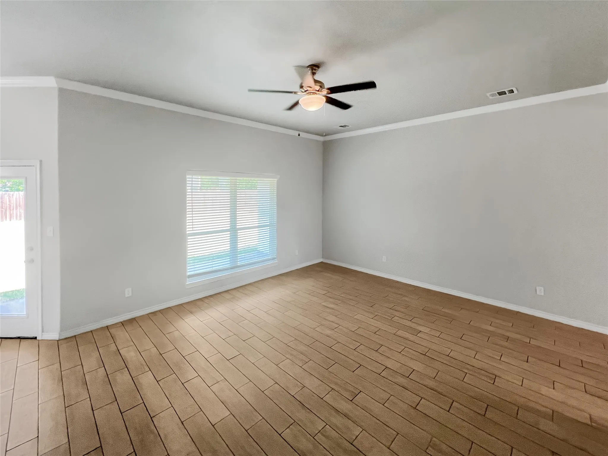 Spacious interior featuring wood-look tile flooring, crown molding, and a ceiling fan with integrated lighting
