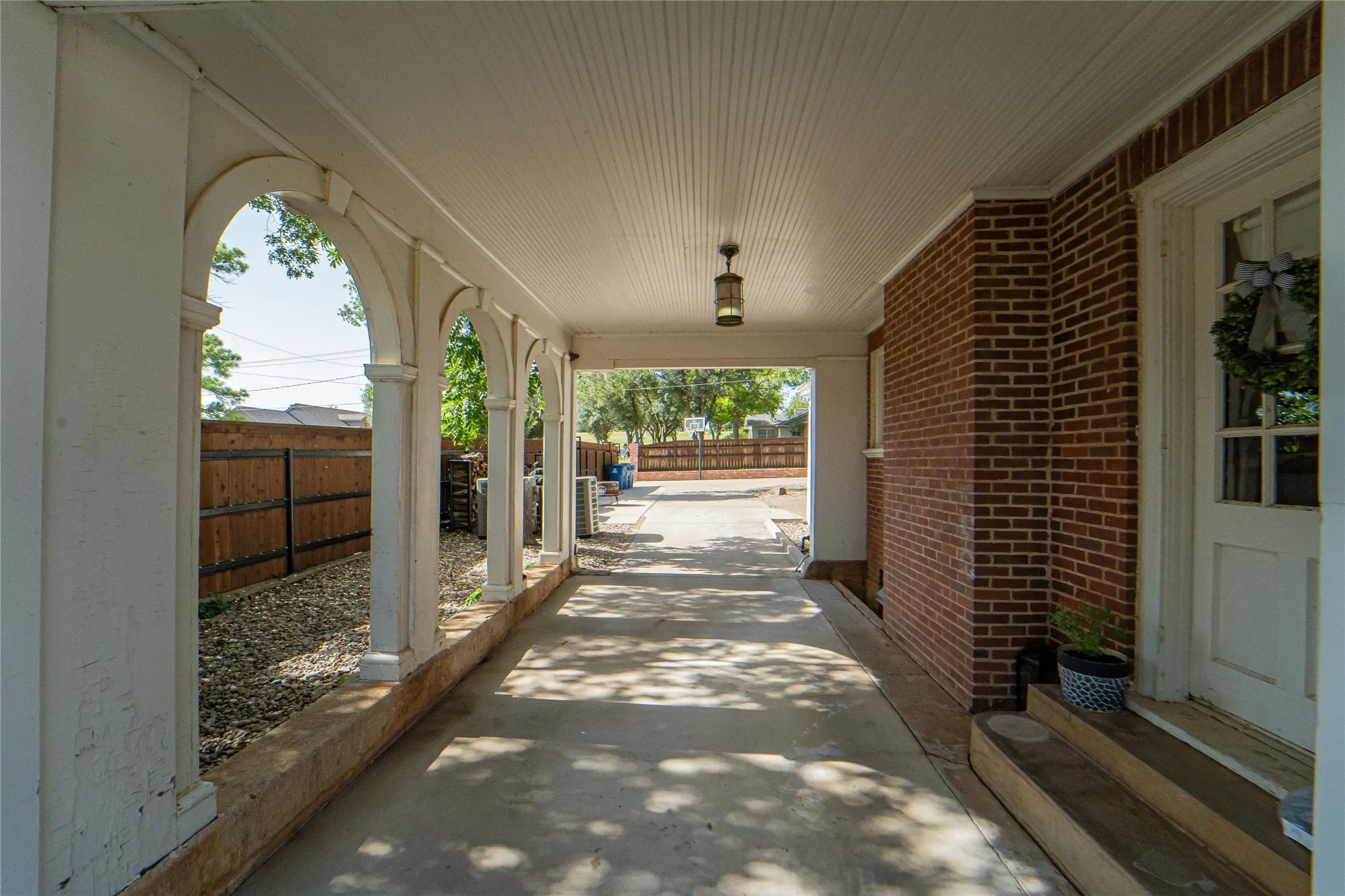 Covered carport and walkway with arched supports, featuring brick exterior, beadboard ceiling, and a concrete surface
