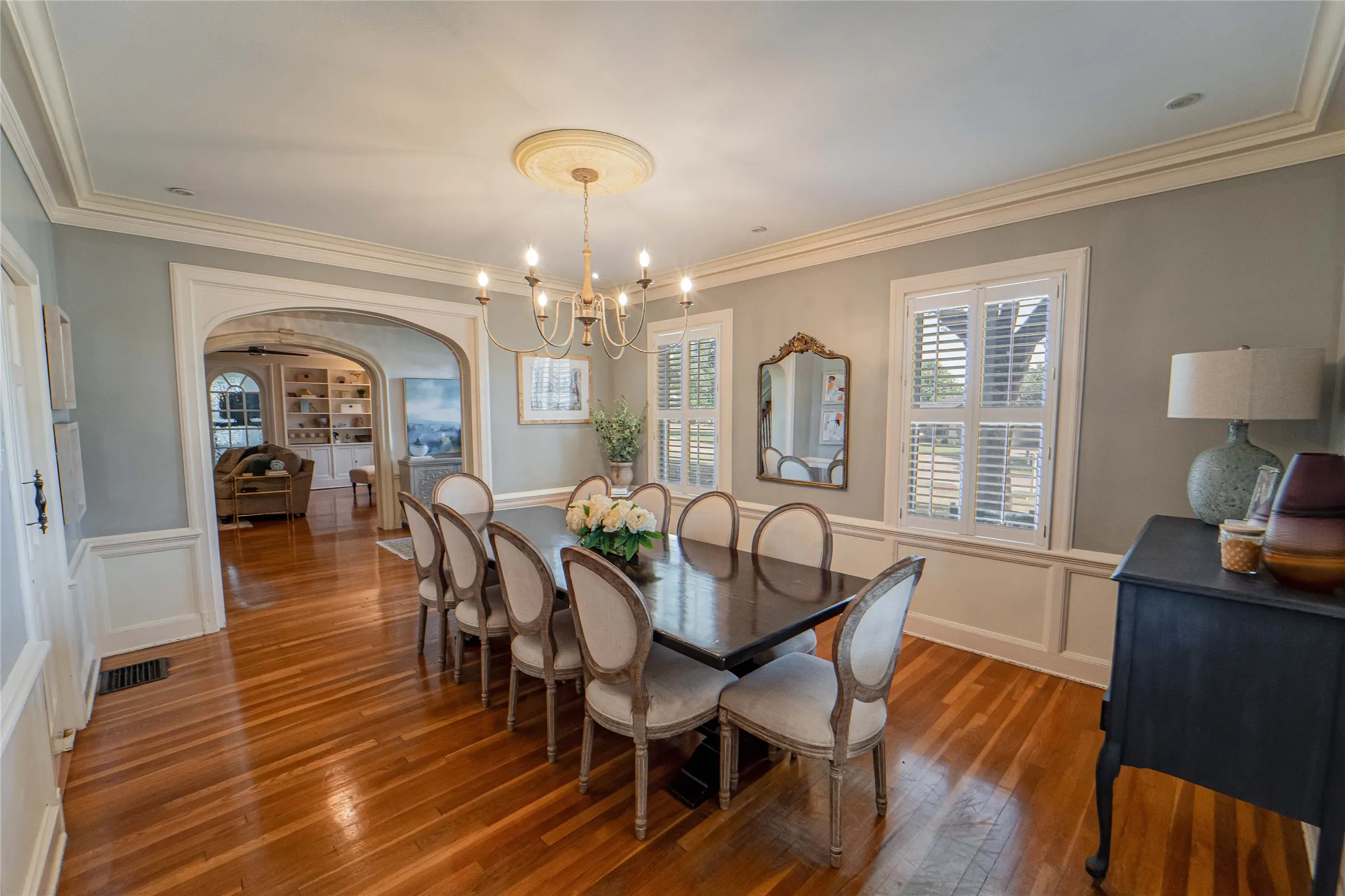 Inviting room featuring wood-finish flooring, an arched entryway, detailed crown molding, built-in shuttered windows, and wainscoting
