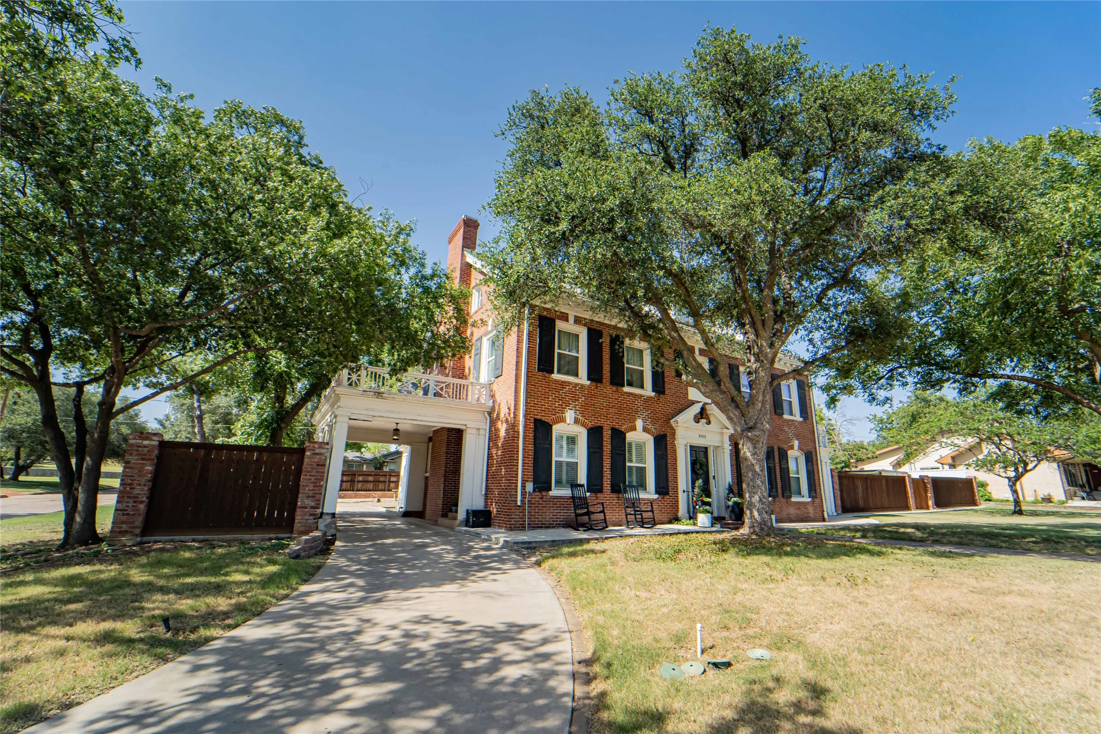Traditional brick exterior featuring a portico, white columns, and black louvered shutters