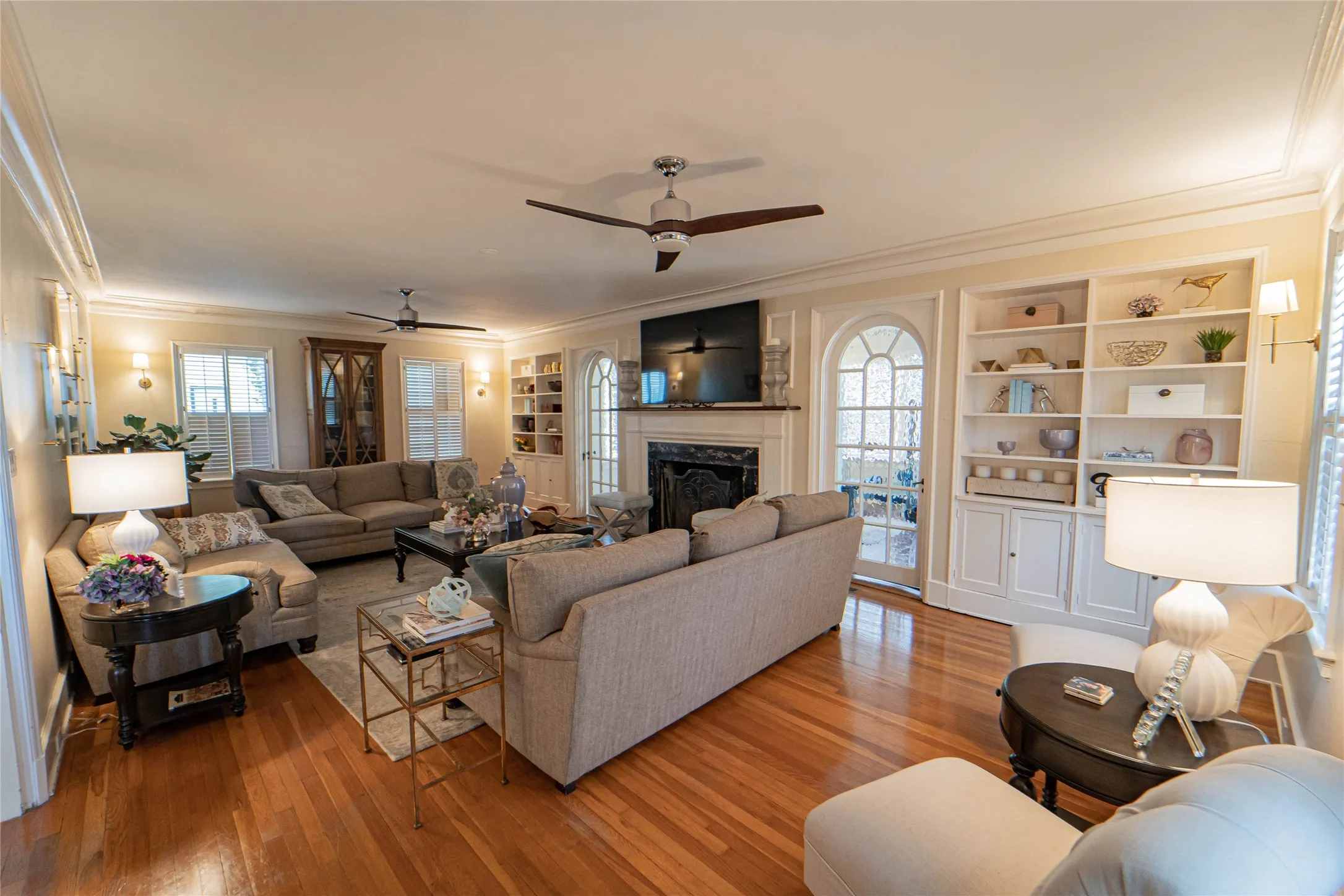 Spacious living area featuring wood-finish flooring, a fireplace with a dark stone hearth, built-in shelving, and an arched glass-panel door