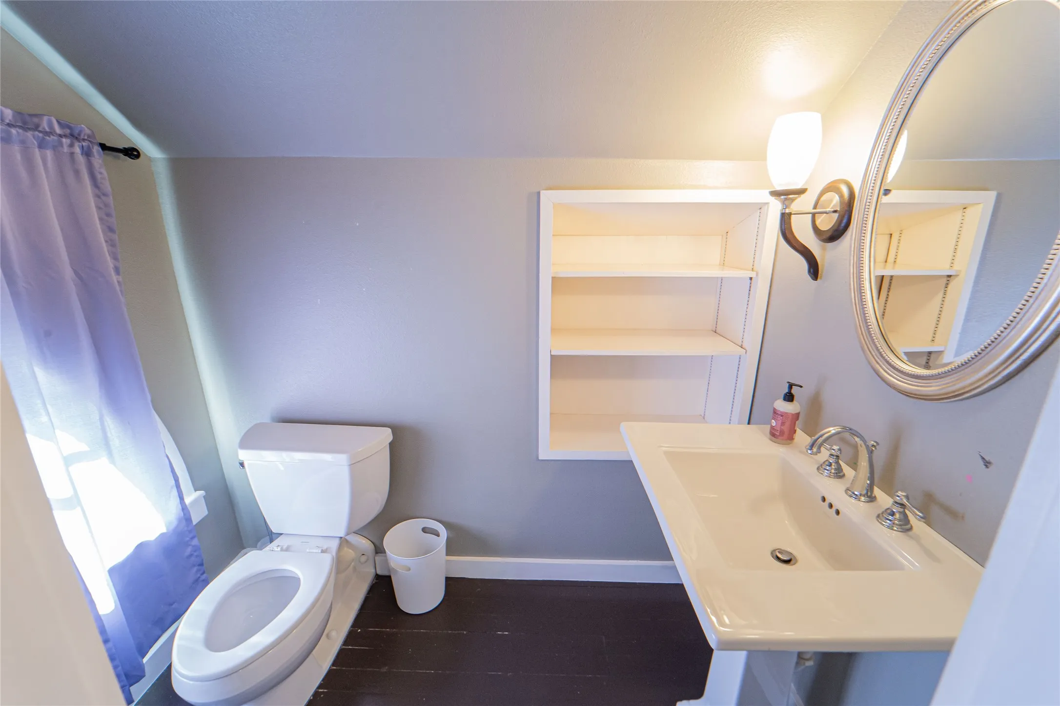 Bathroom with wall-mounted sink, built-in shelving, two-piece toilet, and dark wood-finish flooring