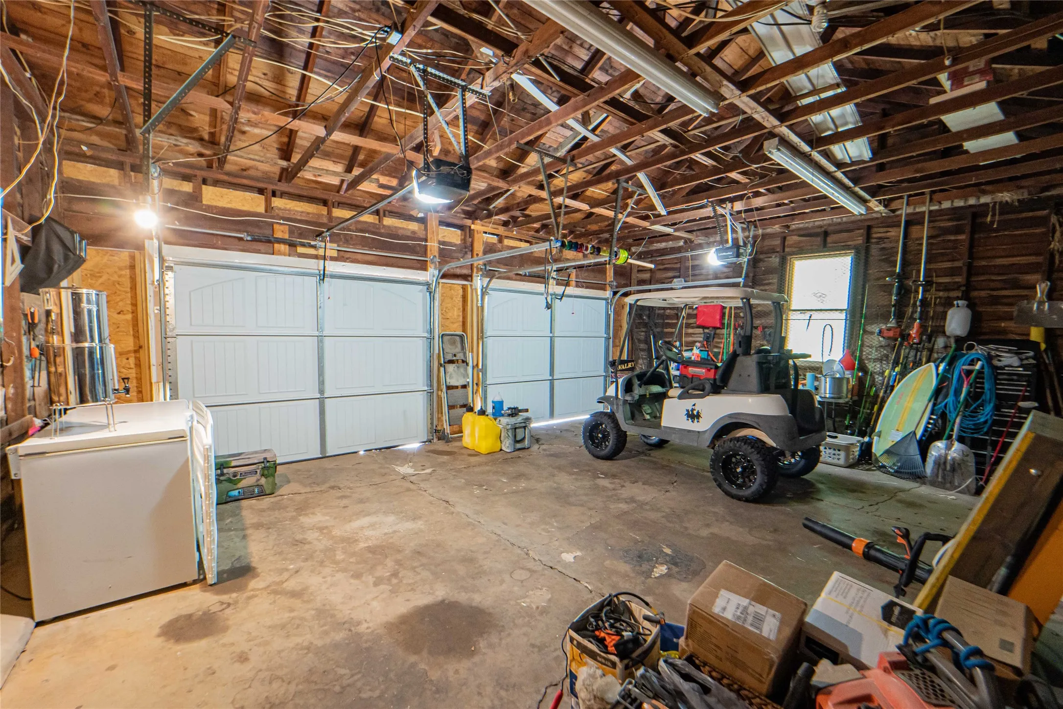 Spacious garage with exposed wood beam ceiling, concrete flooring, and two paneled garage doors with automatic openers