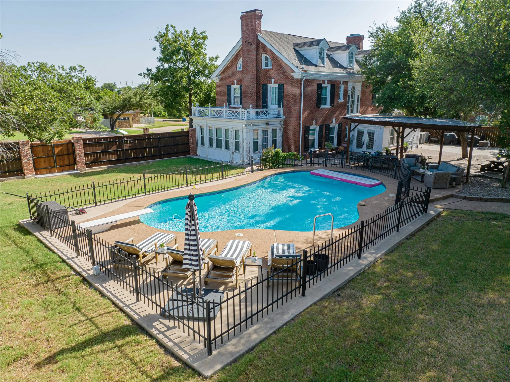 Brick exterior residence with a private swimming pool featuring a diving board, surrounded by a black wrought iron fence