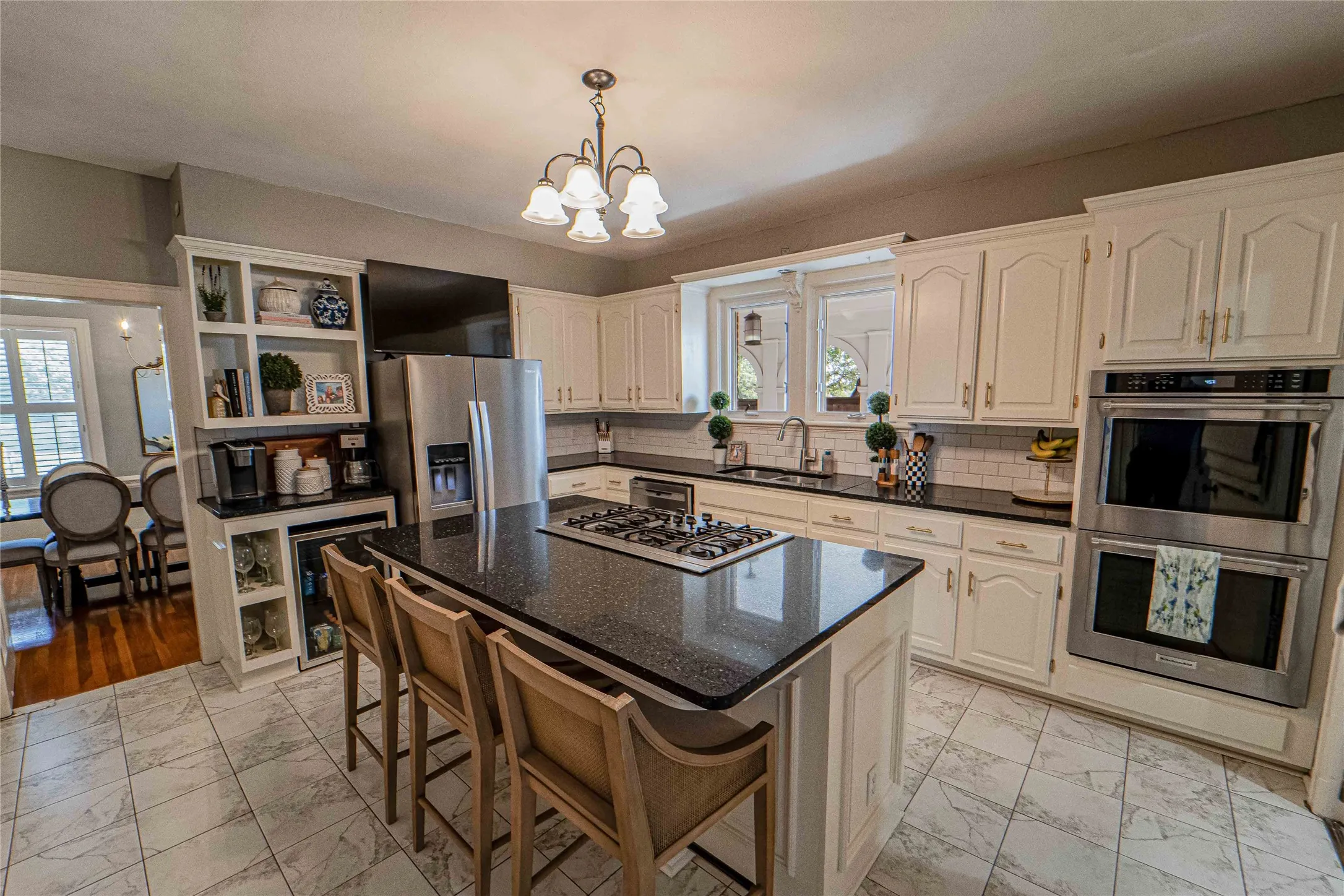Spacious kitchen featuring an island with a gas cooktop, double wall ovens, built-in shelving, white cabinetry, and tile flooring