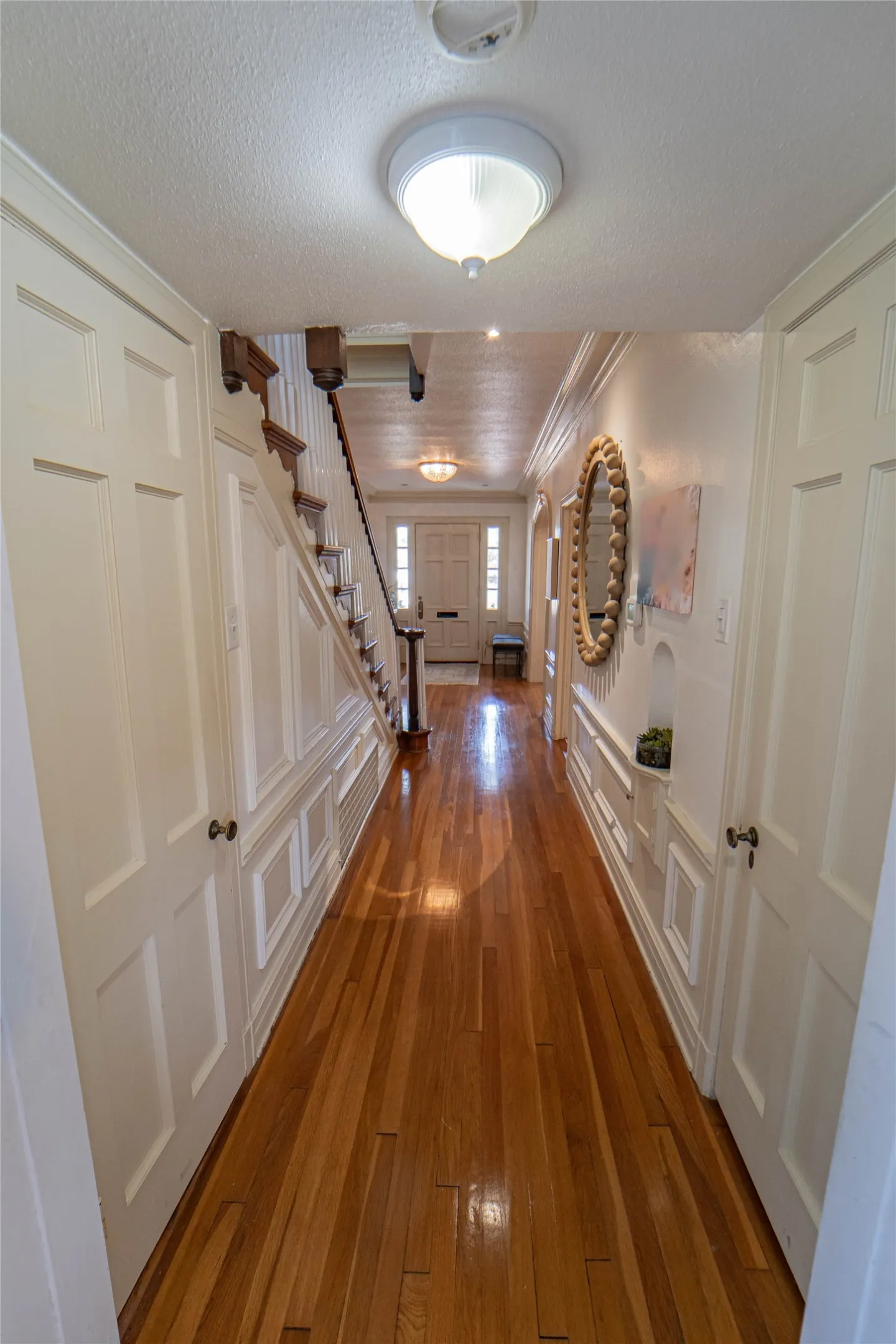 Long hallway featuring wood-finish flooring, wainscoting, and a staircase with a dark wood handrail